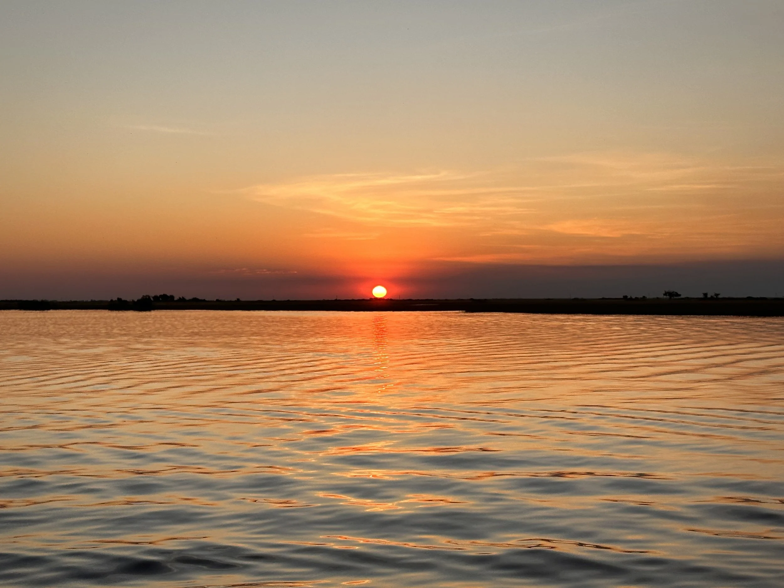 Sunset over the Zambezi River near Victoria Falls, with calm water and colorful sky reflections.