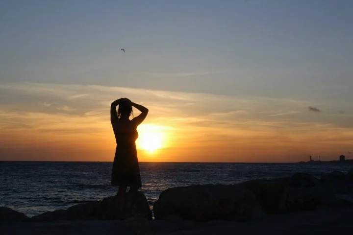 Silhouette of a woman standing on coastal rocks during sunset in Curaçao, Caribbean island ocean view.