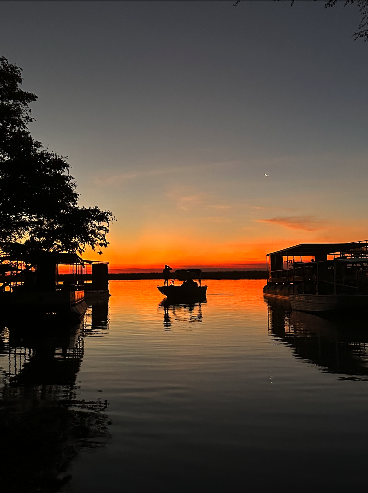 Sunset cruise on the Chobe River in Botswana with boats reflecting on calm water under a crescent moon