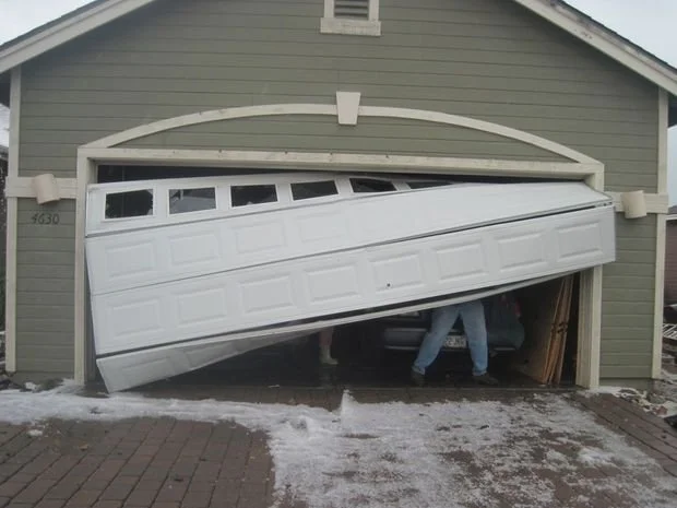 A garage door damaged and tilted inward, resembling a garage door that looks like it is falling or malfunctioning, with people working underneath.