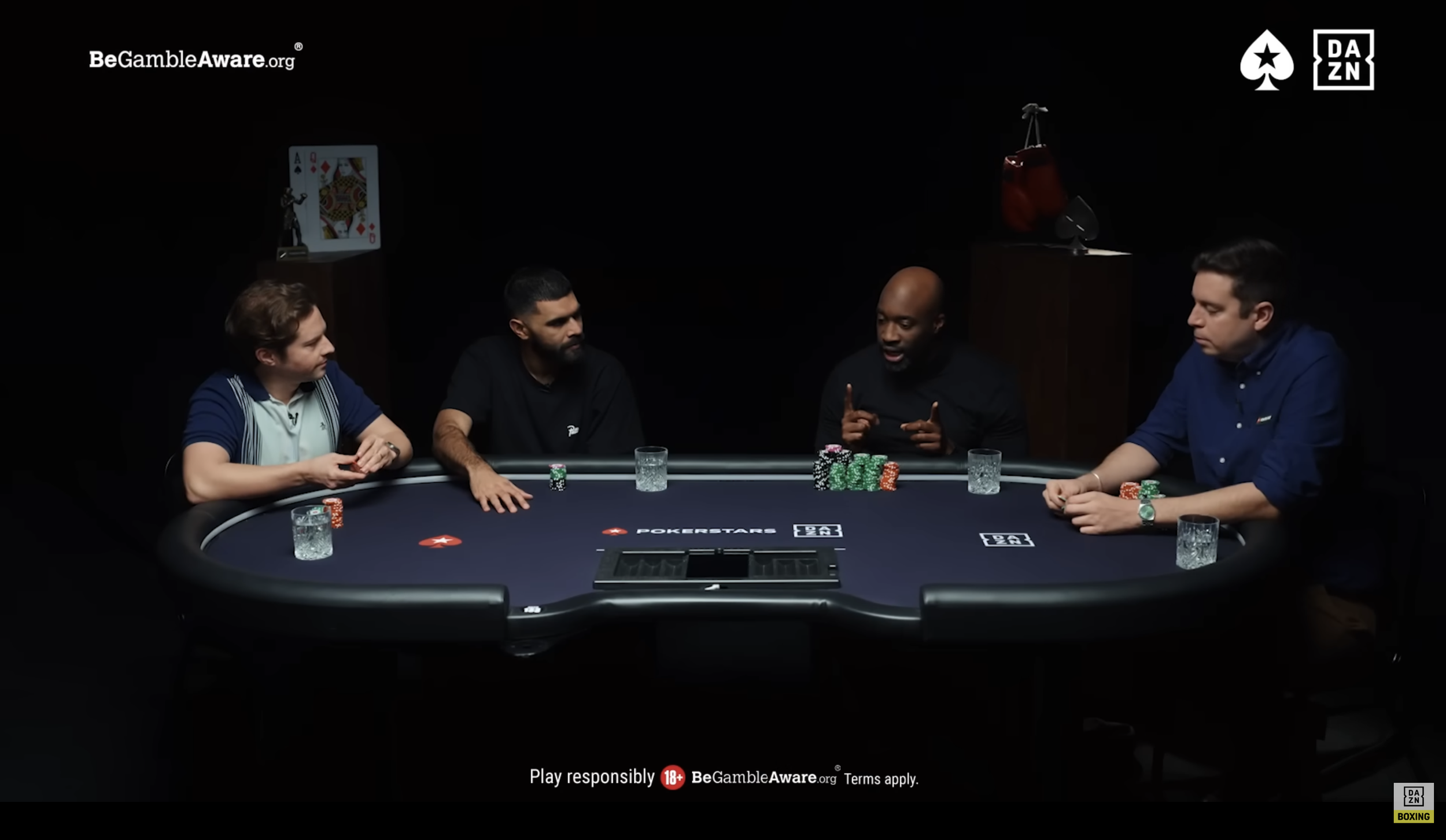 Four men sit around a poker table engaged in a game. There are poker chips and glasses of water on the table. Judging by the logo, the scene is in a professional or televised setting, with a dark background and minimal lighting focused on the players and the table.