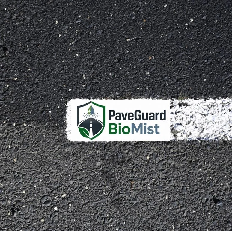A close-up of a rejuventation treatment on an asphalt pavement with a white parking line and a sticker that reads 'PaveGuard BioMist' with a logo of a shield and a leaf.