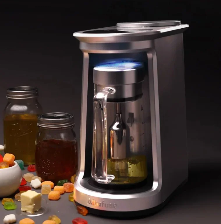 A modern essential oil diffuser with a glass bottle inside, emitting a blue mist, surrounded by jars of colored liquids and scattered gummy candies on a dark surface.