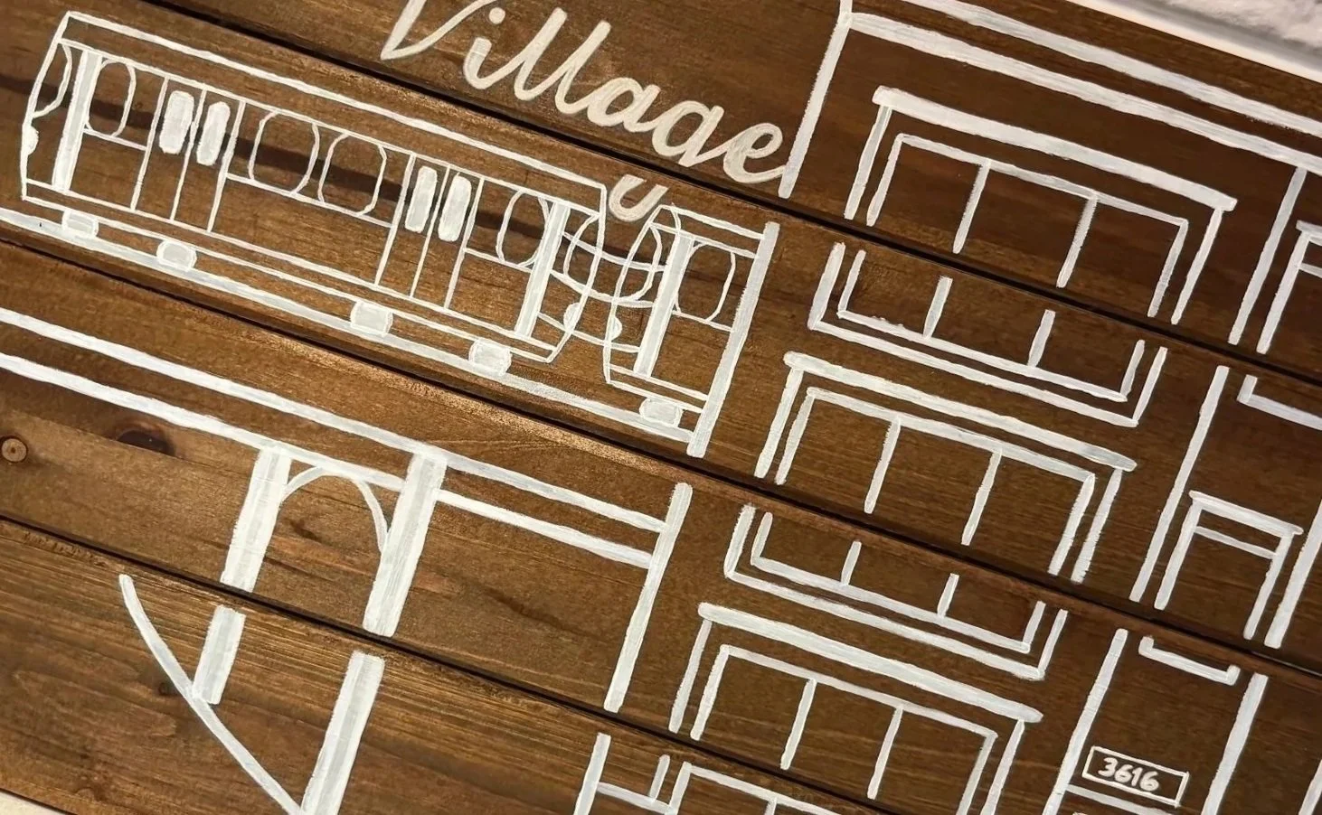 Wooden wall art with white hand-painted outlines of a house with multiple windows, a door, and the words 'Villa de' written at the top, and the number '3616' at the bottom right corner.