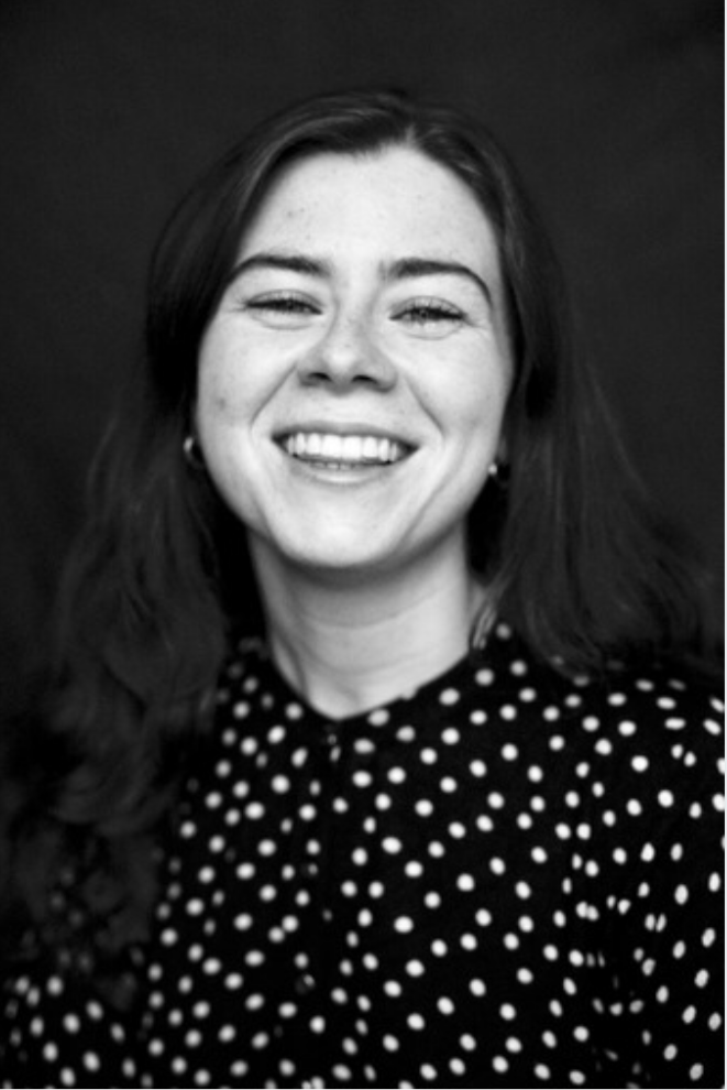 Black and white portrait of a woman with long dark hair, smiling, wearing a polka dot top, and small hoop earrings.