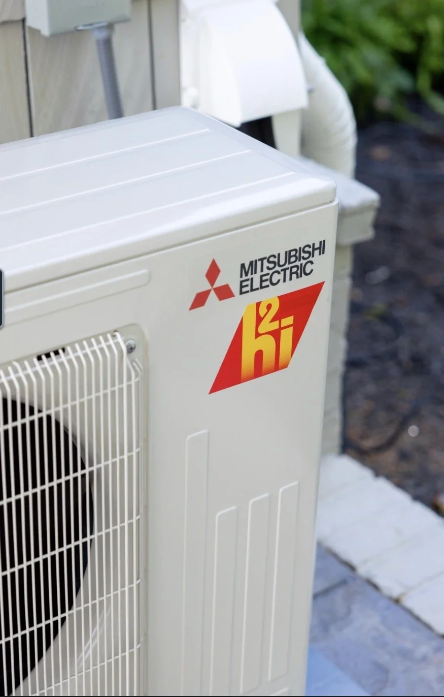 Outdoor Mitsubishi Electric air conditioning unit with a red and yellow Hi 2 logo sticker.