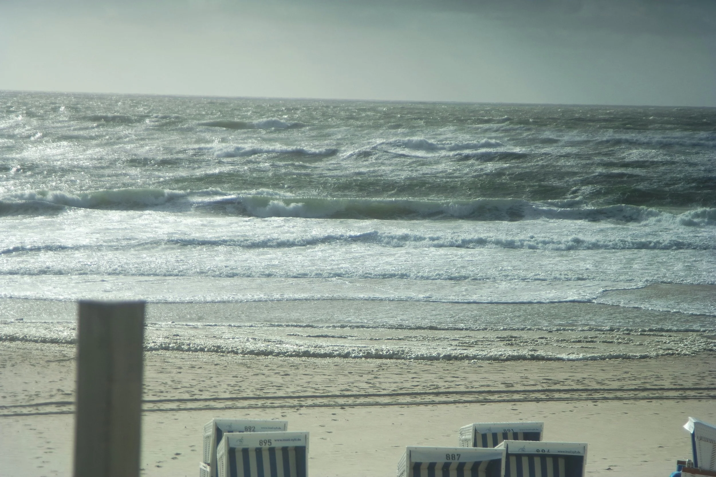 A beach with sand and waves in the ocean, with a few empty striped lounge chairs.