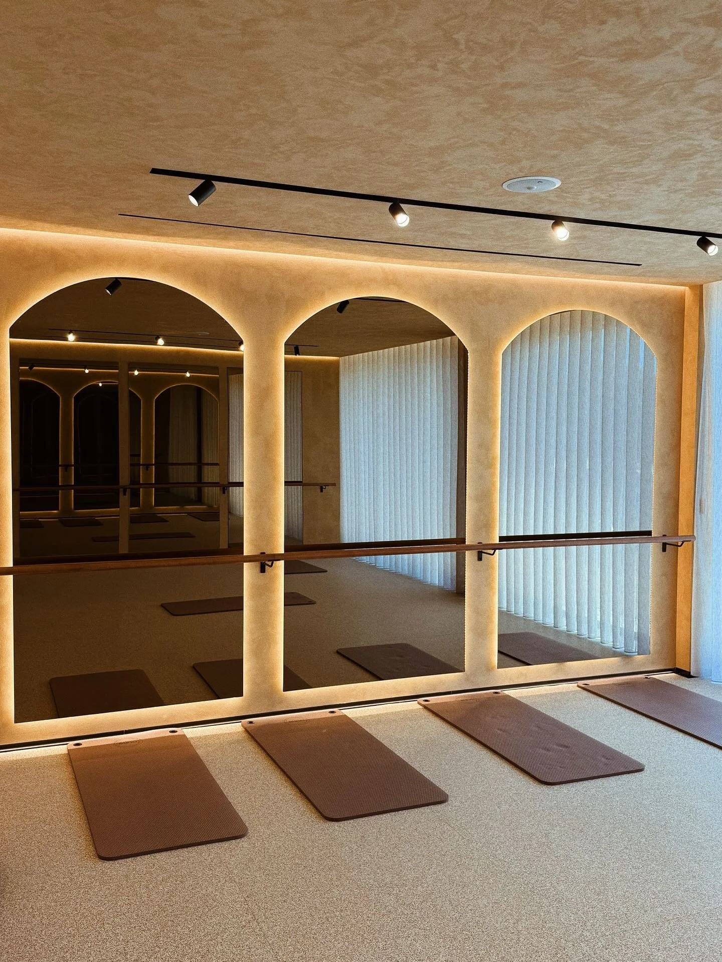 Sala de yoga com espelhos, tapetes de yoga e barras para alongamento, com iluminação suave e cortinas de vidro.