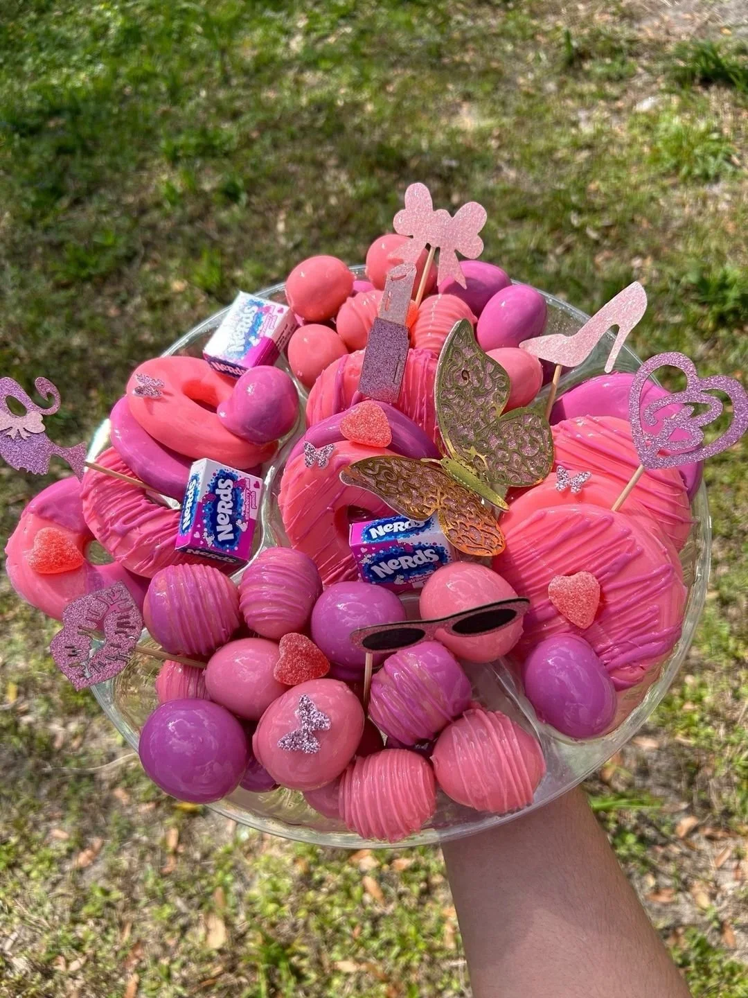 A bouquet of pink and purple candies, chocolates, and decorative paper butterflies and hearts. Some candies are wrapped, and there are small Nerolaps chocolates.