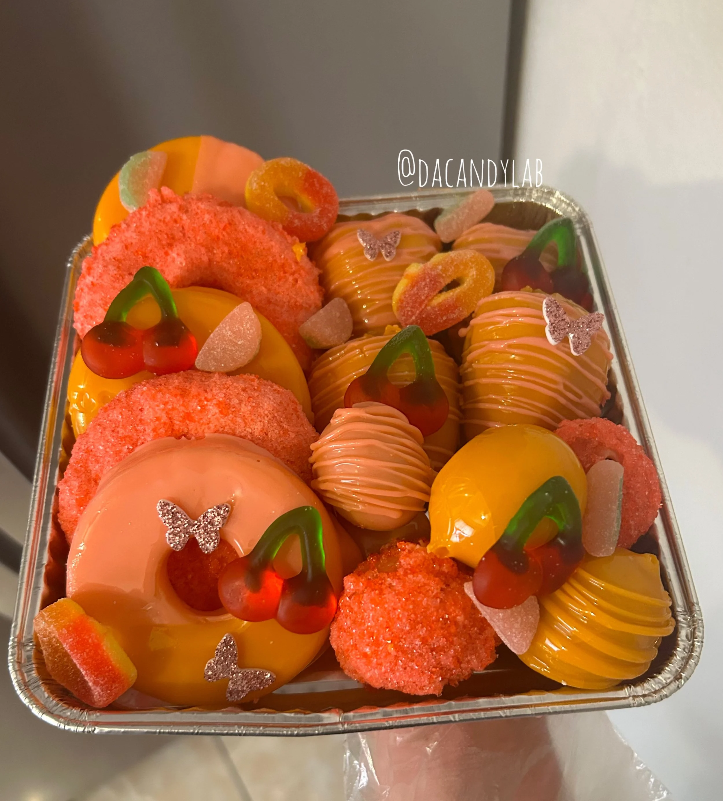 A tray of colorful Halloween-themed candies and decorations, including gummy worms, caramel apples with drizzle, gummy bears, and decorative butterfly and pumpkin shapes.