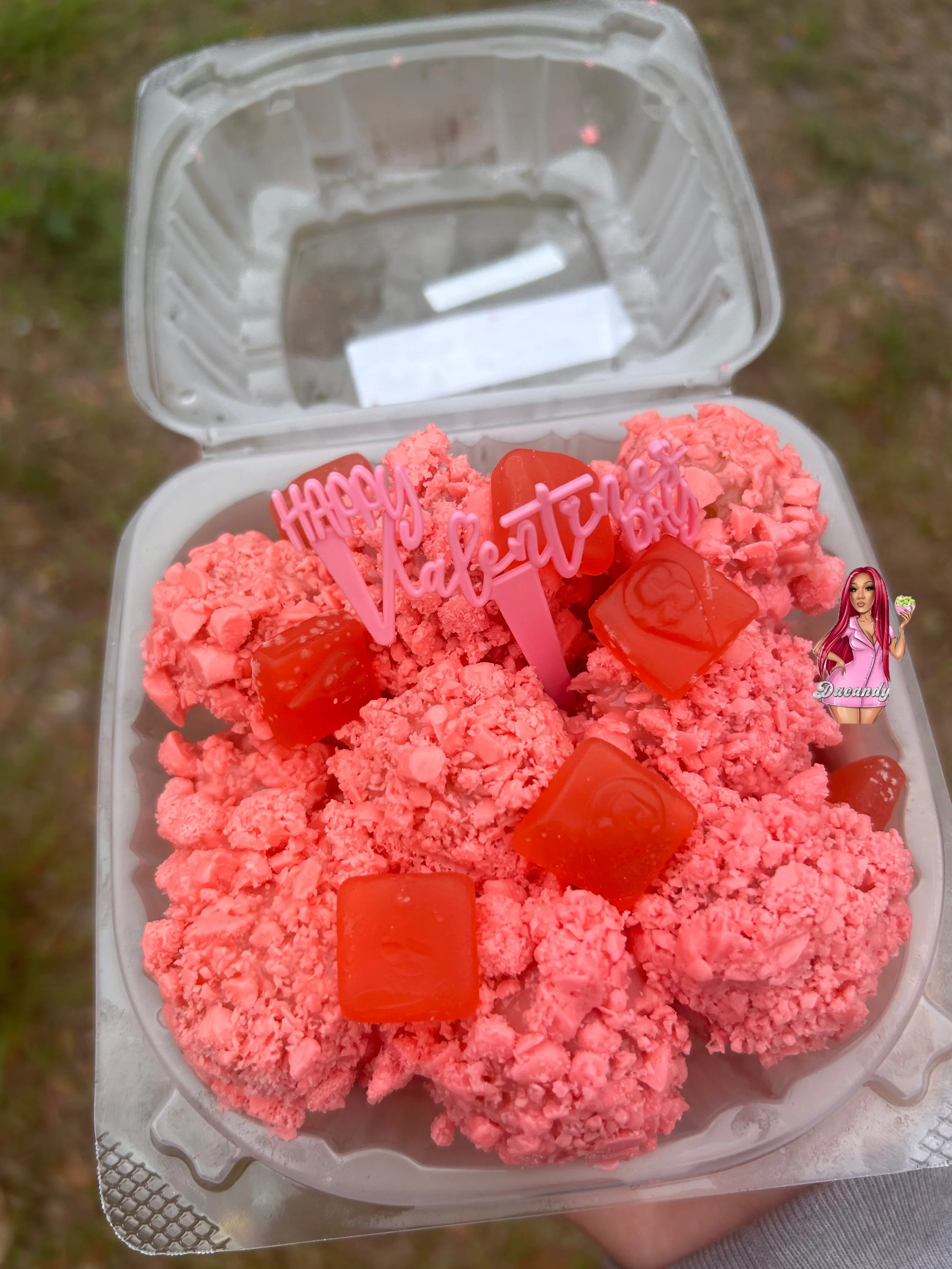 Container of pink-colored dessert balls topped with red candy cubes and a pink 'Happy Valentine's Day' pick, with an artificial woman figure on the side.