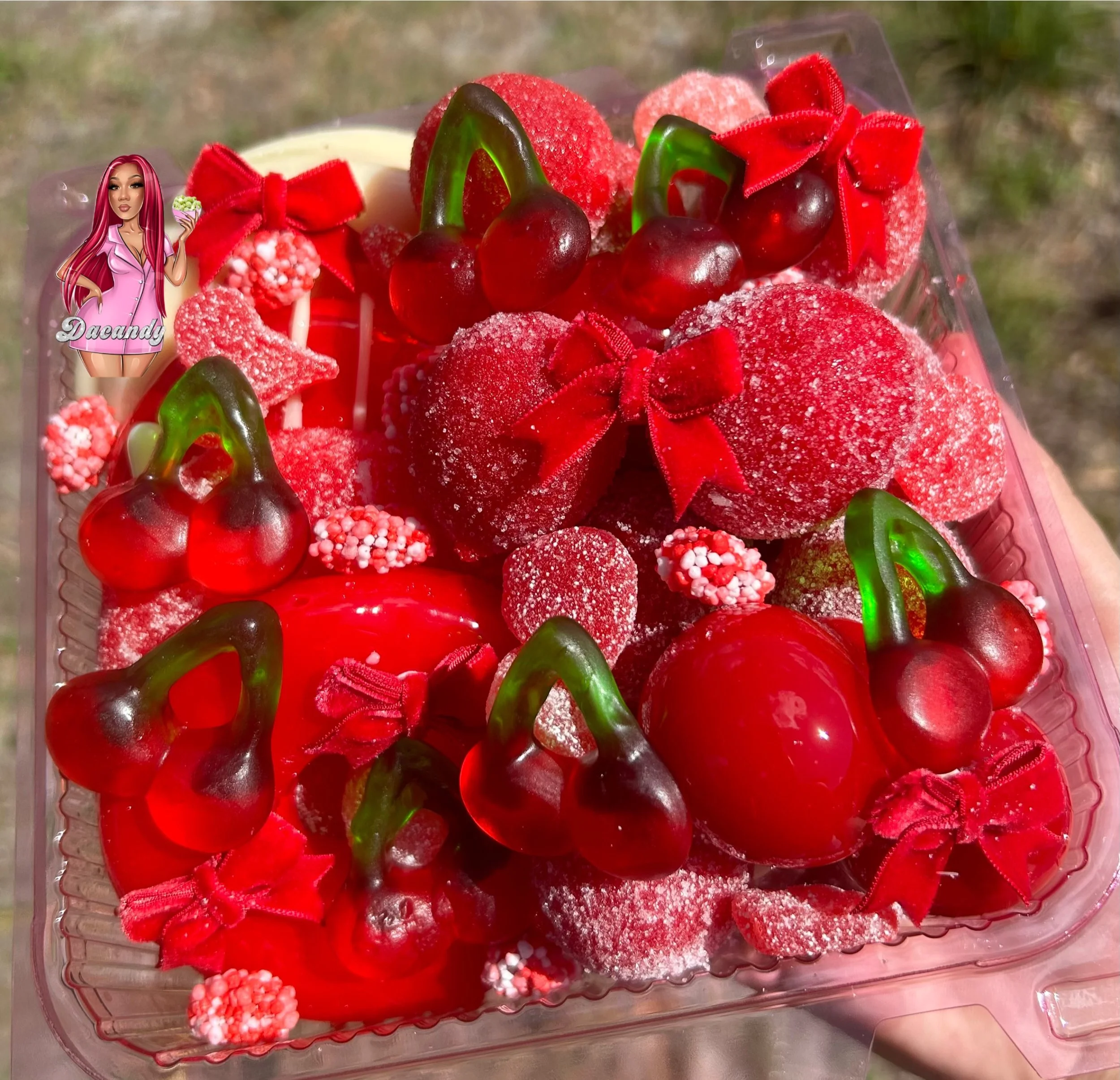 Red-colored decorated cookies with cherries, bows, and sugar crystals, arranged in a tray.