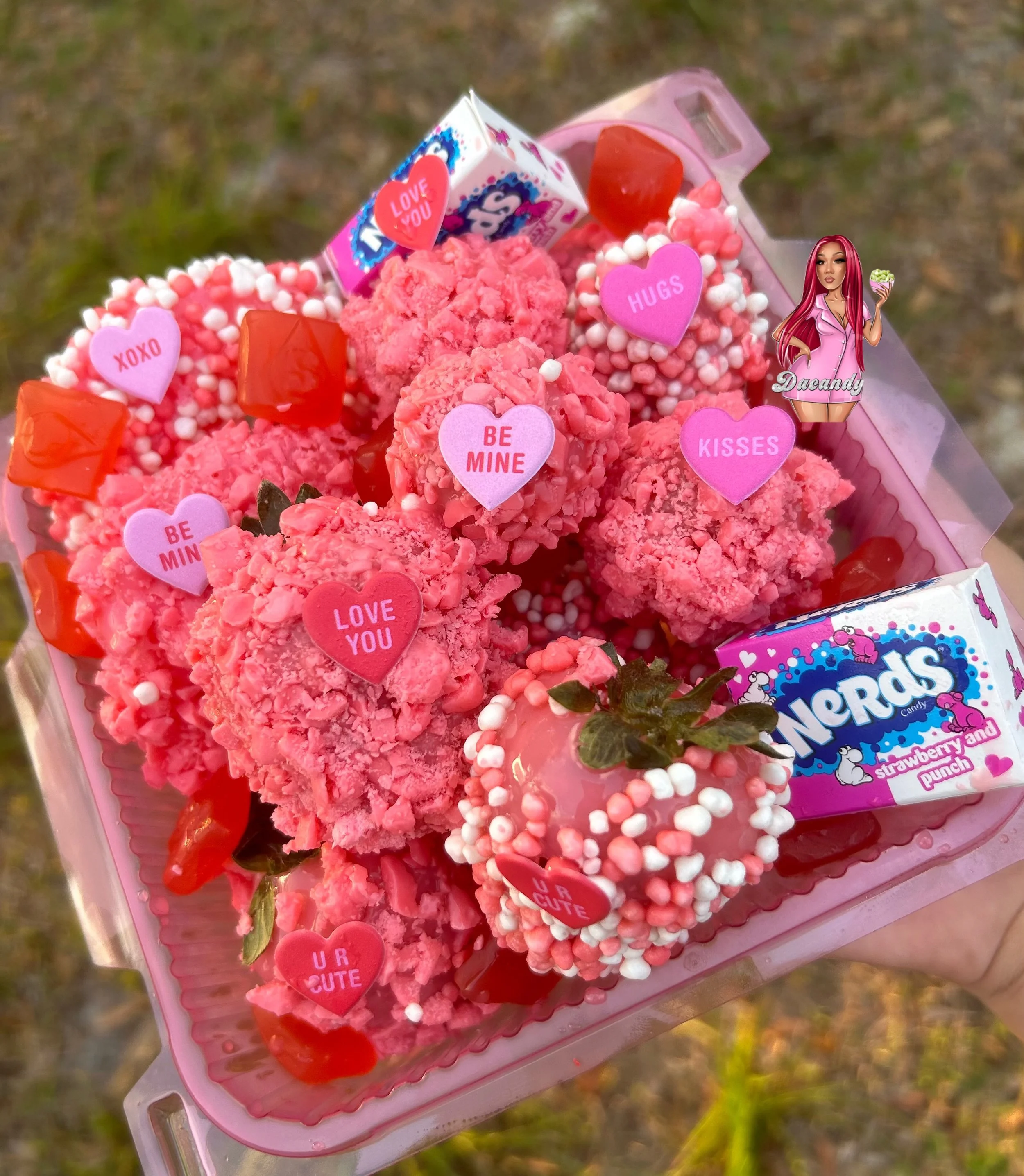 A pink tray filled with strawberry and punch-flavored candies, decorated with heart-shaped stickers with messages such as "LOVE YOU," "BE MINE," "HUGS," "KISSES," and "XOXO," along with a small chocolate box and strawberries.