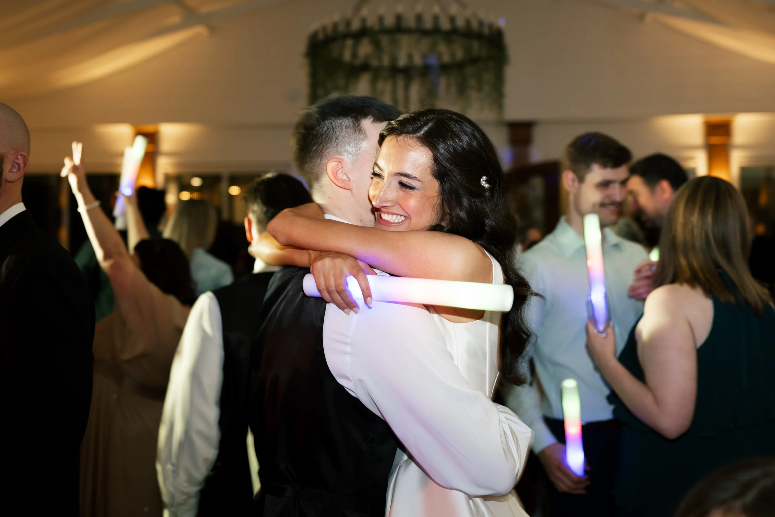 A bride and groom hugging on the dance floor, being celebrated by their closest friends and family dancing.