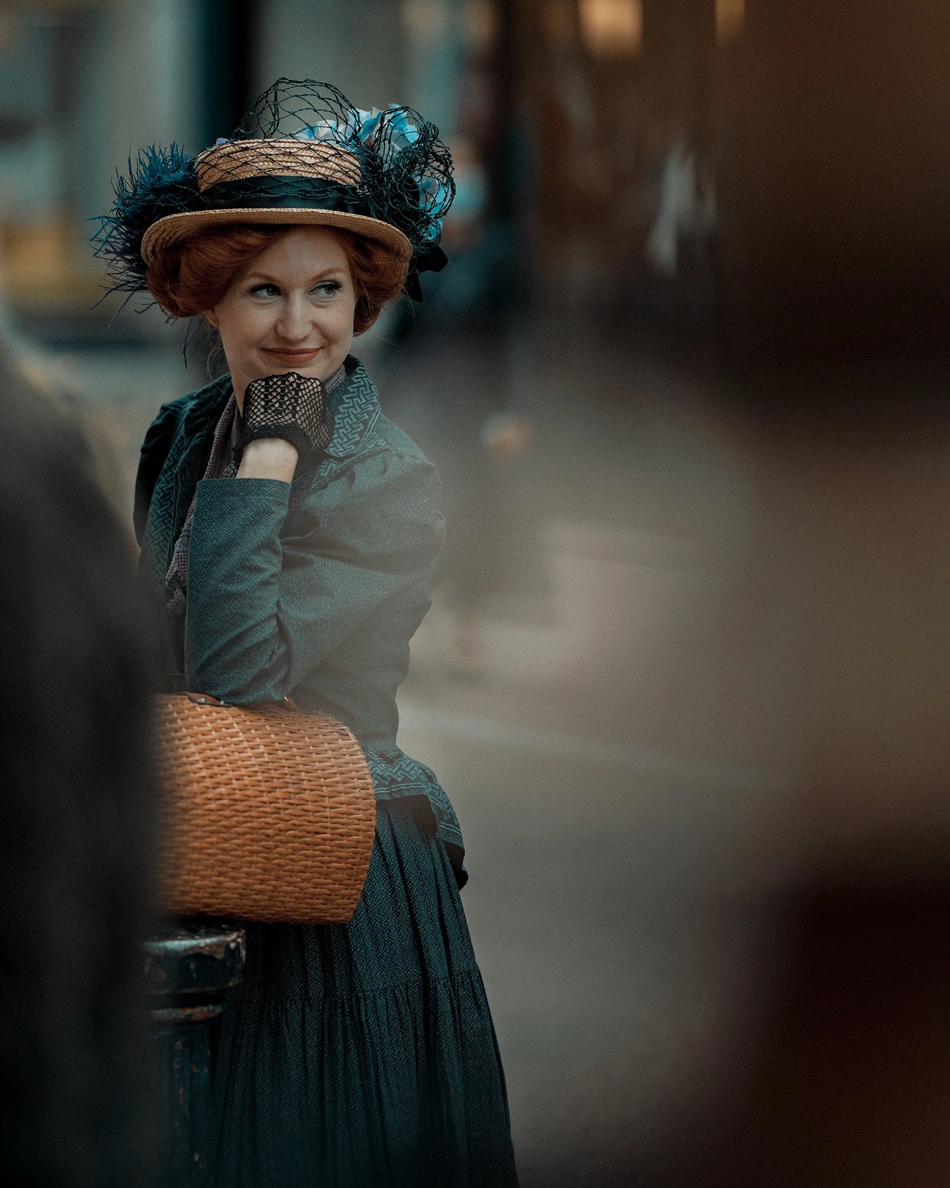 Candid Dublin street portrait of a smiling woman in a vintage hat with blue feathers, leaning on an orange bag - Photo by Daniya