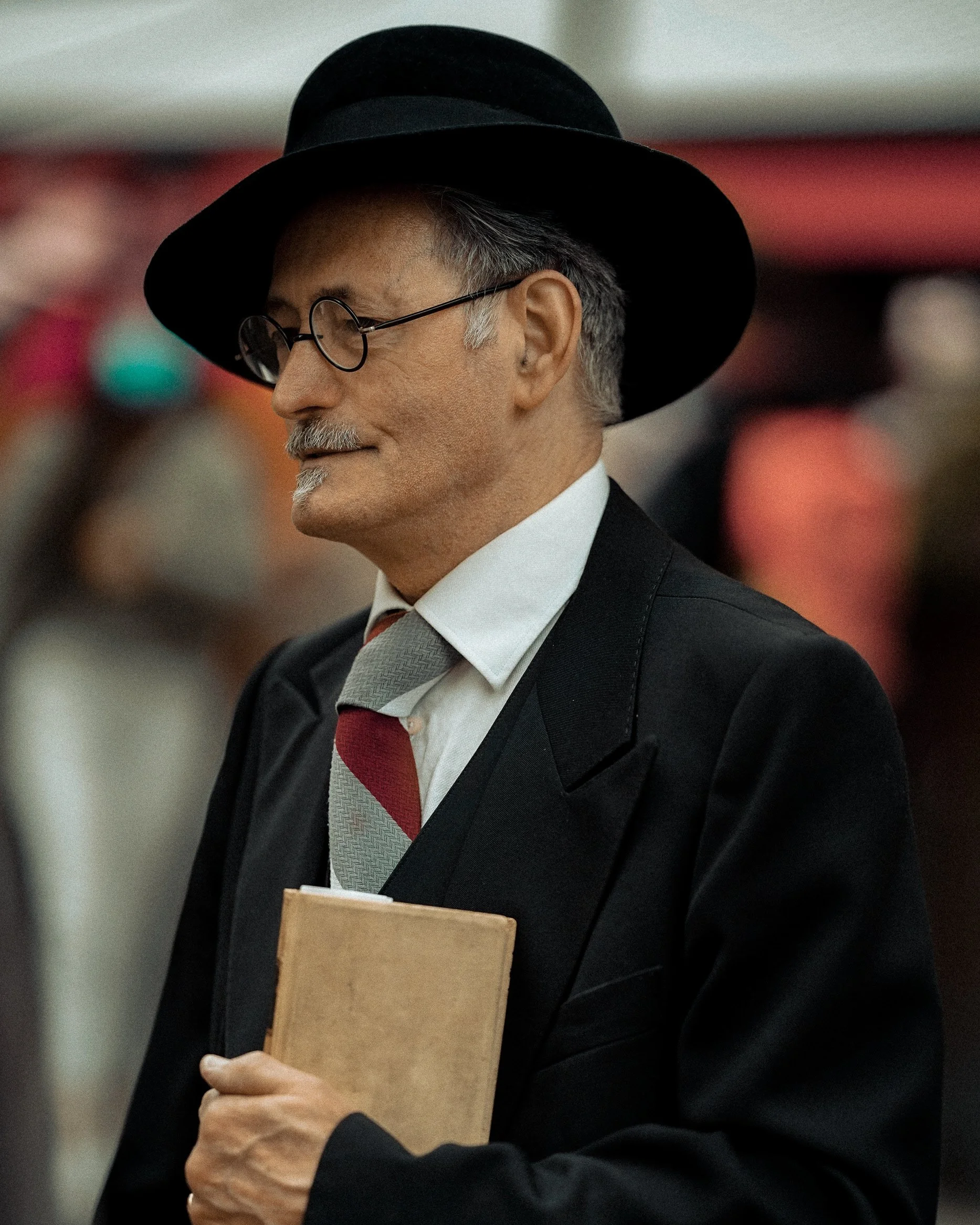 Candid Dublin street portrait of an older man in a black hat and suit, holding a book, with a thoughtful expression- photo by Daniya