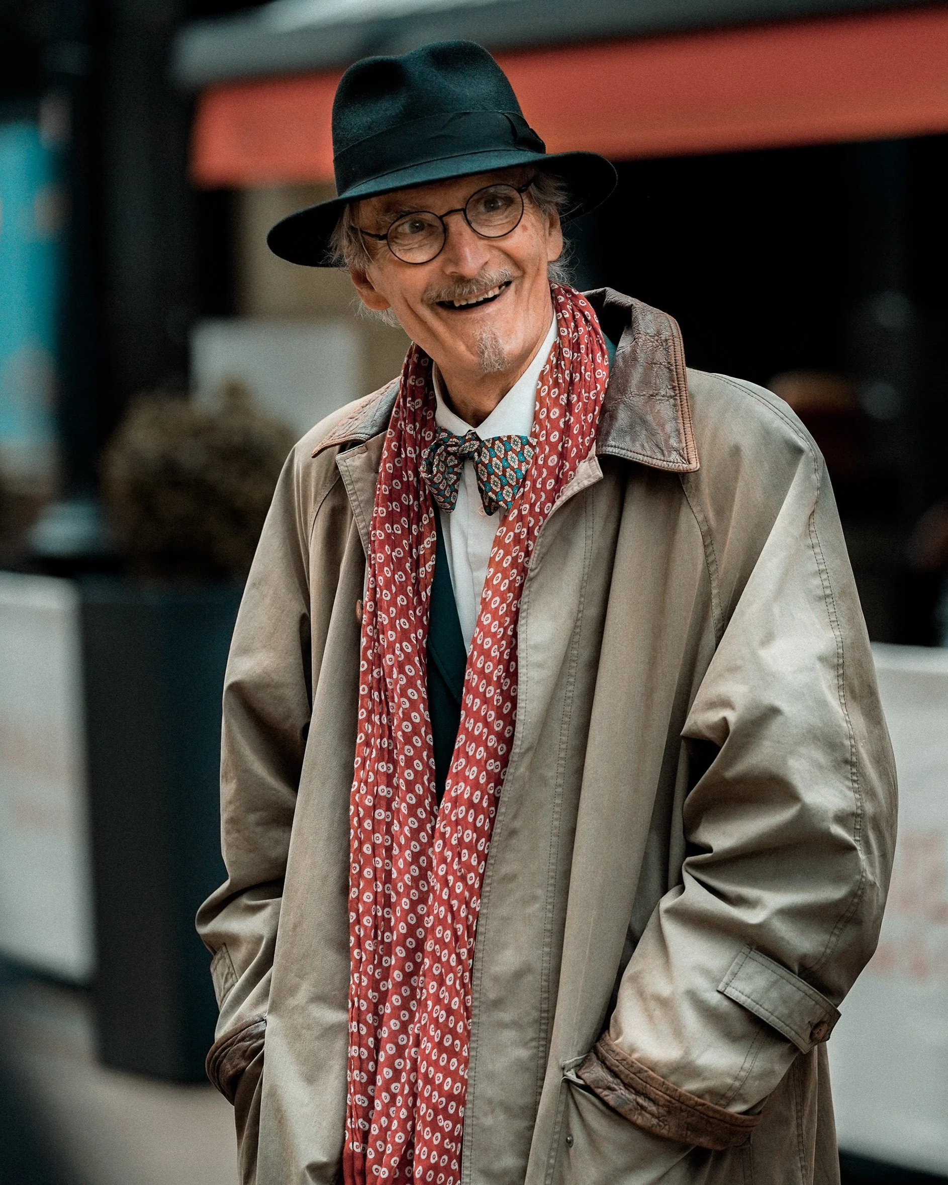 Candid Dublin street portrait of an older man smiling, wearing a black hat, glasses, beige coat and red scarf – Photo by Daniya, street photography