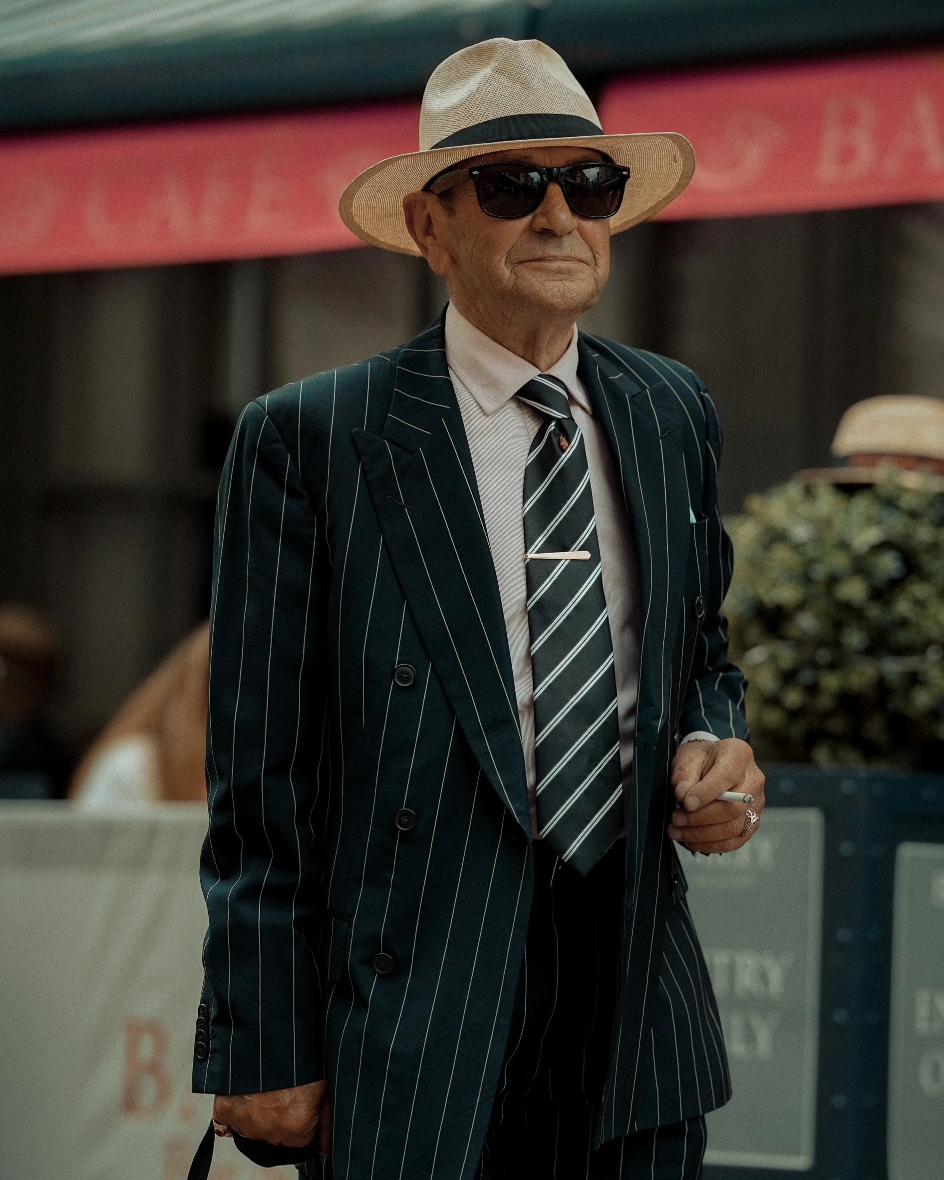 Stylish Dublin street portrait of a man in a pinstripe suit, sunglasses, and light hat, candid moment – Photo by Daniya, street photography.
