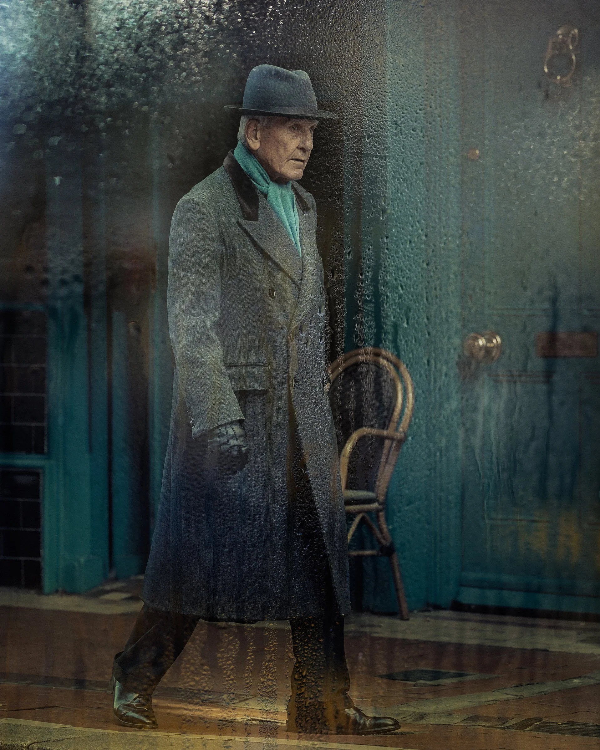Stylish man in a grey coat and black hat walking past a rain-streaked window, moody tones — Dublin street photography, Photo by Daniya.
