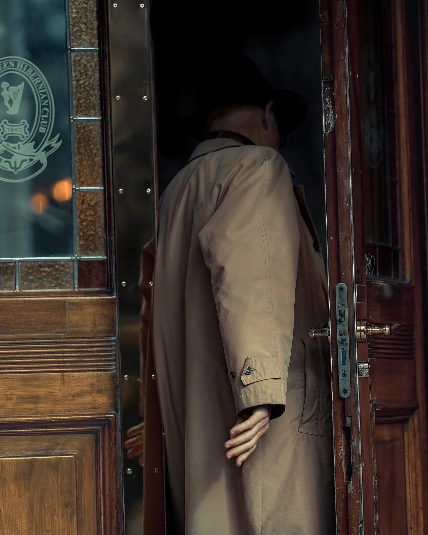 Man in a beige coat stepping into a wooden doorway, cinematic candid moment — Dublin street photography, Photo by Daniya.