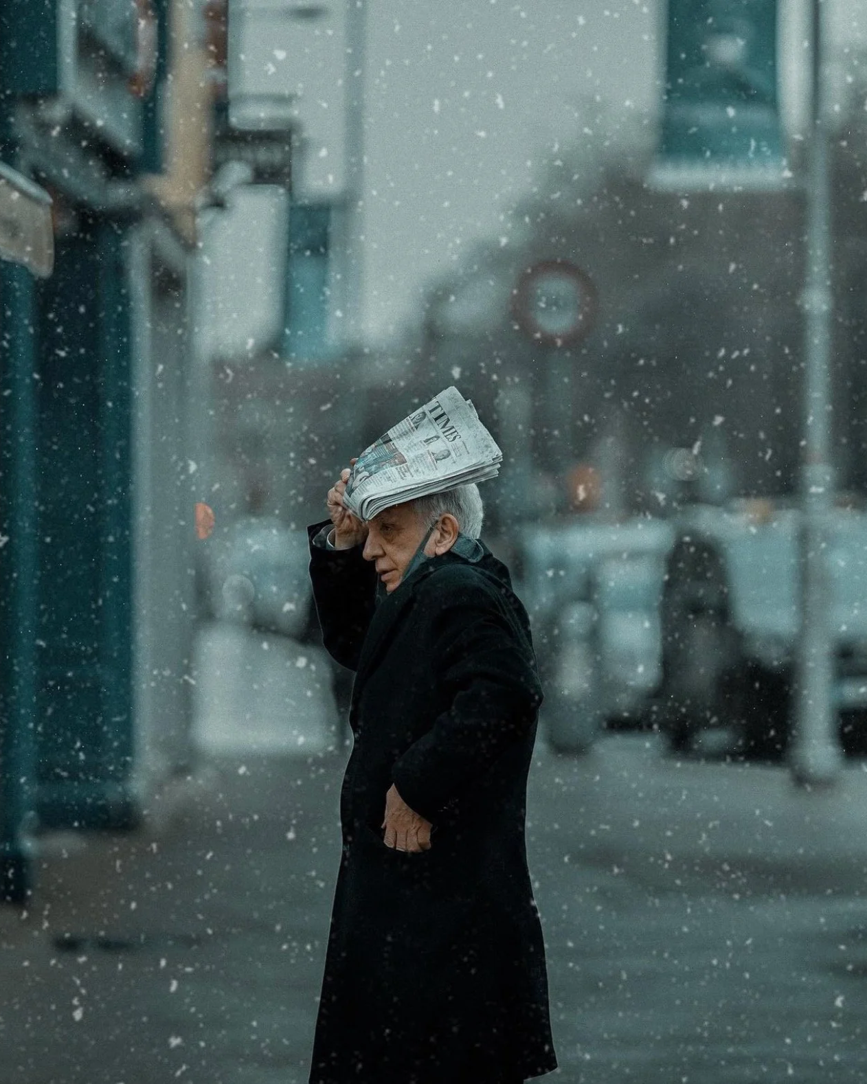 Person in a black coat using a newspaper to shield from the snow, candid city moment — Dublin street photography, Photo by Daniya.