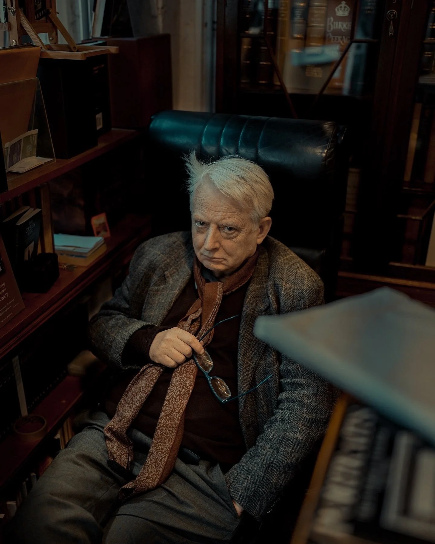 Older man sitting in a vintage library chair, holding glasses with a pensive look — Dublin street photography, Photo by Daniya.