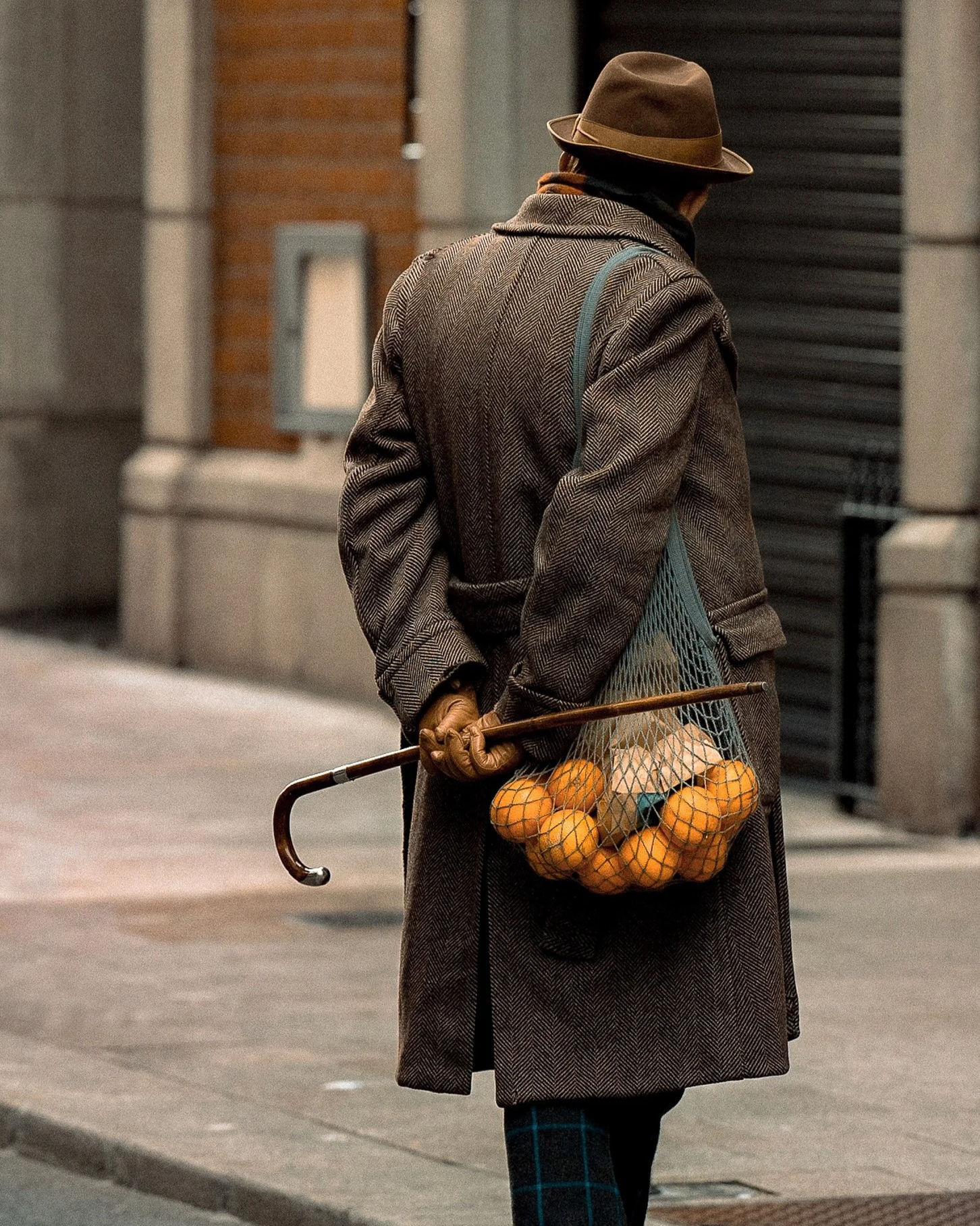 Man in a brown coat and hat walking down the street with a bag of oranges and a cane — Dublin street photography, Photo by Daniya.