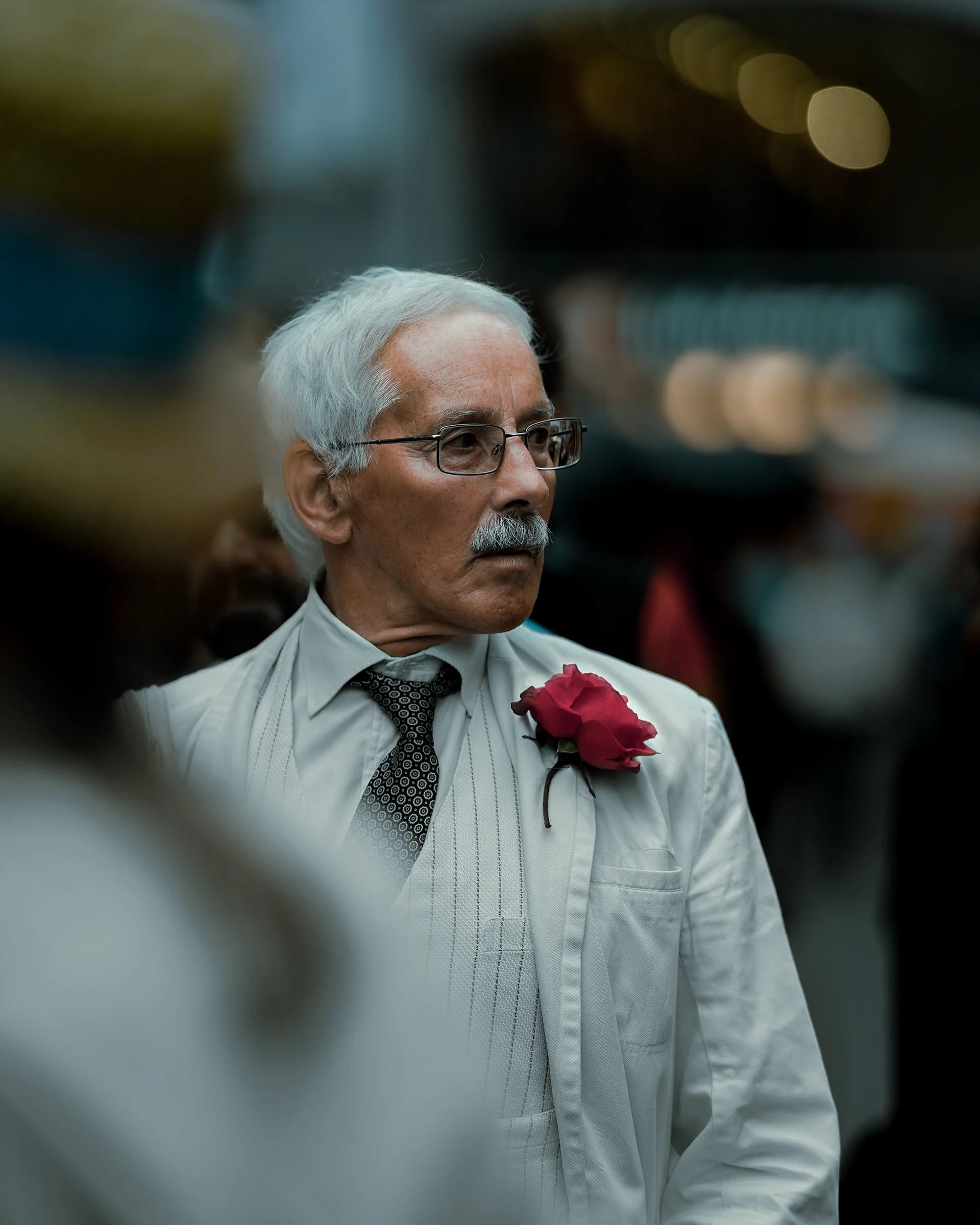 Stylish portrait of an older man in a light suit with a red rose pinned to his jacket, Dublin street fashion photography.