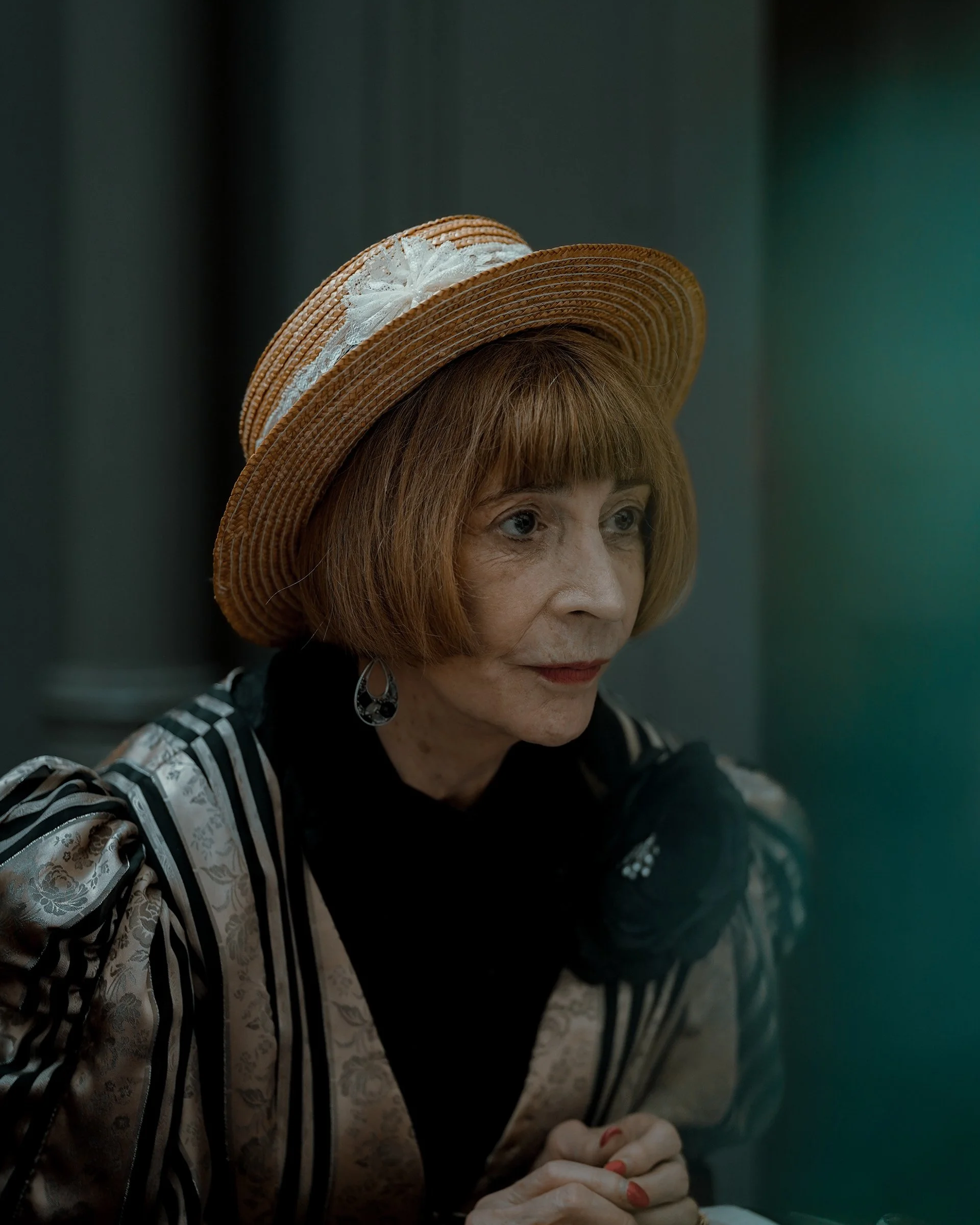 Street portrait of an elderly woman in a straw hat, elegant outfit, and calm expression, Dublin street photography.