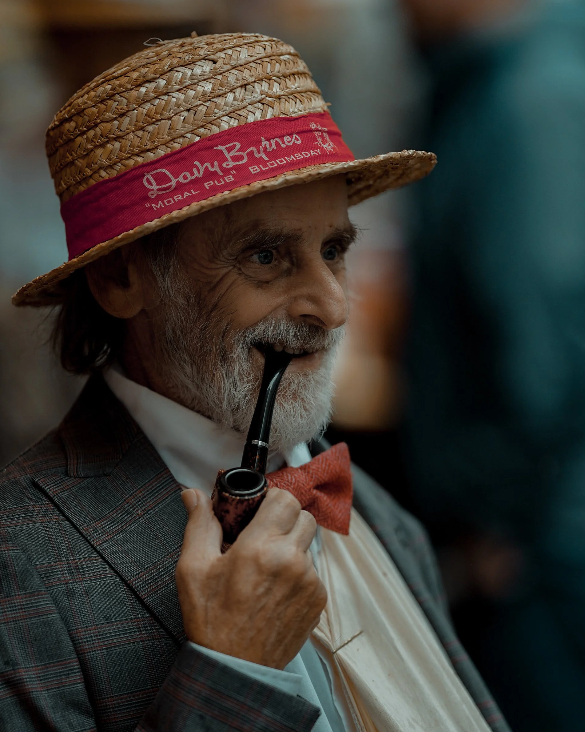 Vintage style portrait of an elderly man in a suit with a red bow tie and straw hat, holding a pipe, Dublin candid photography.