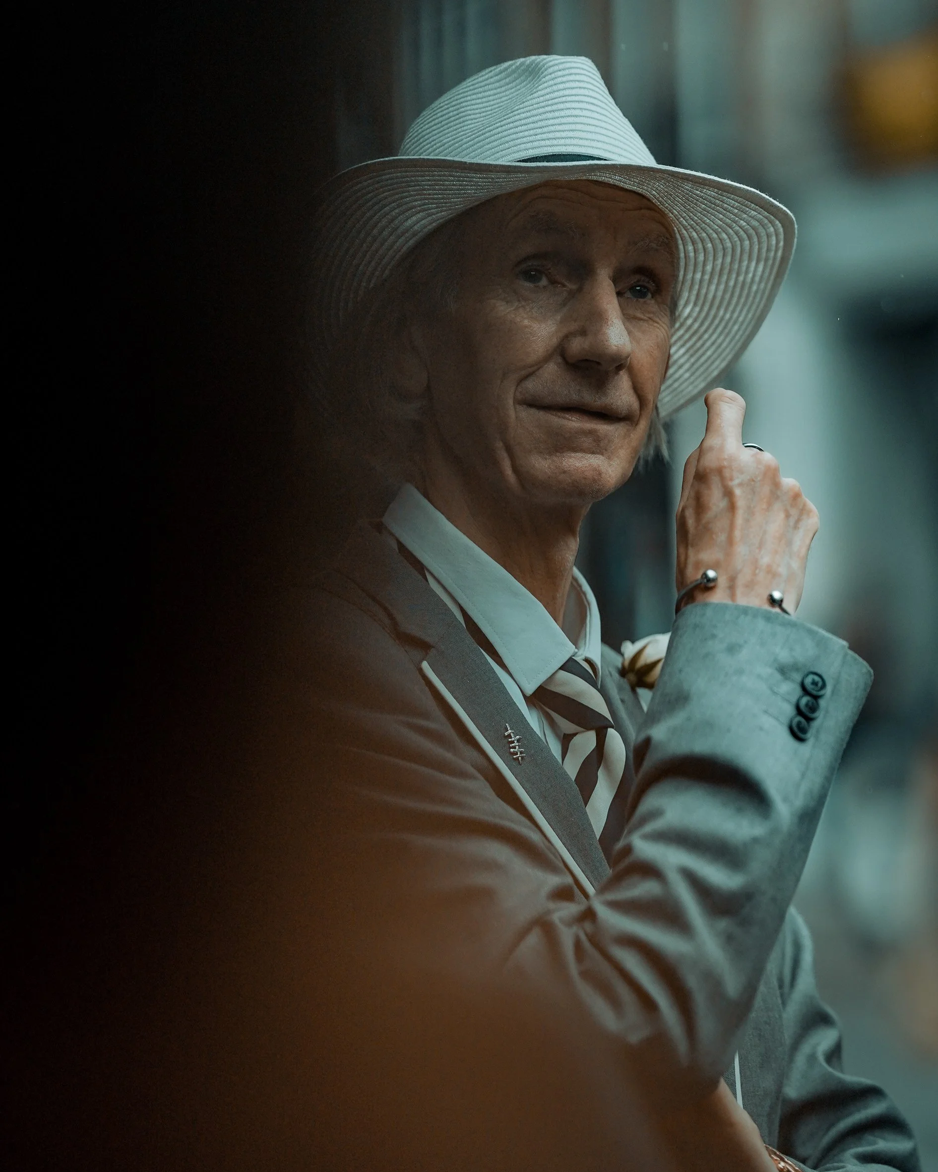 Stylish street portrait of an older man in a grey suit and white hat, giving a slight smile, Dublin street style photography.