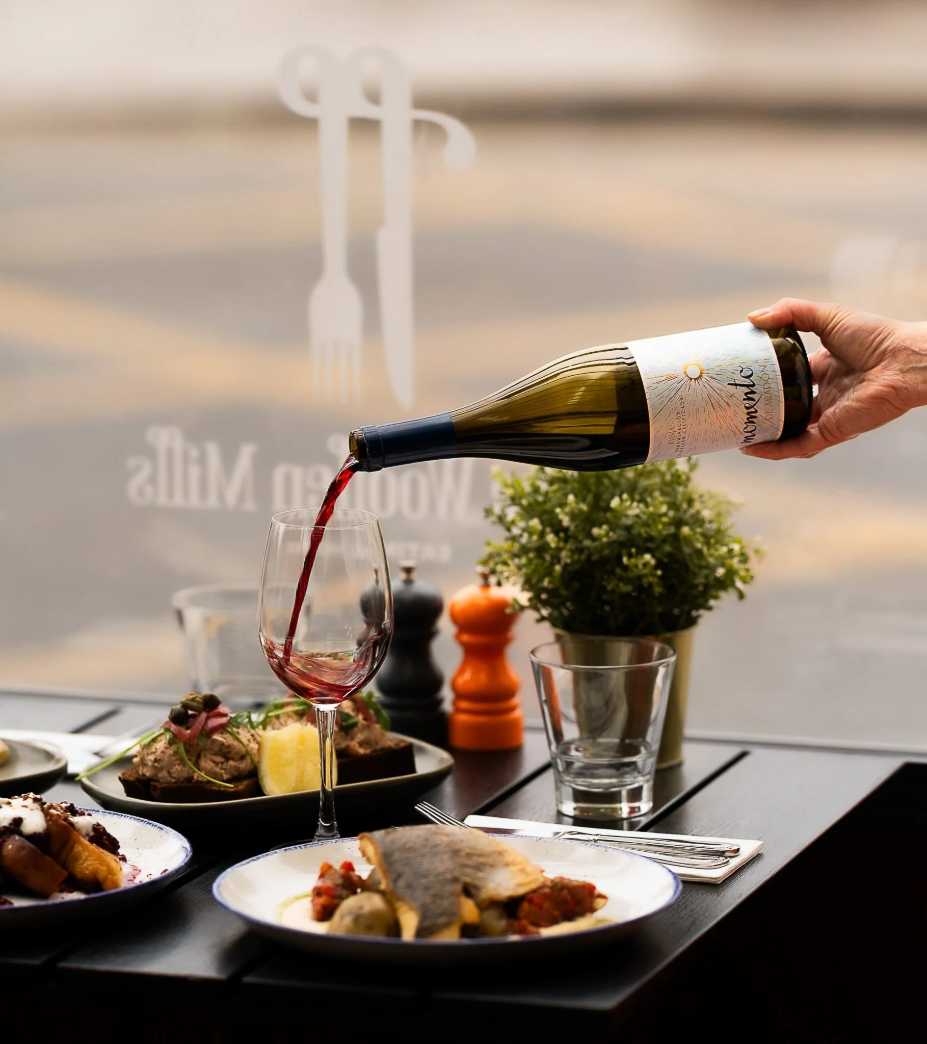 Waiter pouring red wine at outdoor restaurant table.