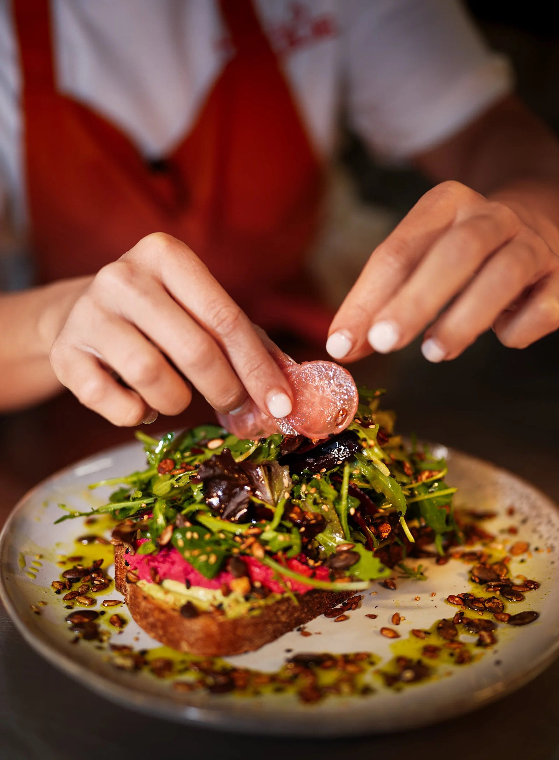 Chef garnishing avocado toast with fresh vegetables in café food photography.