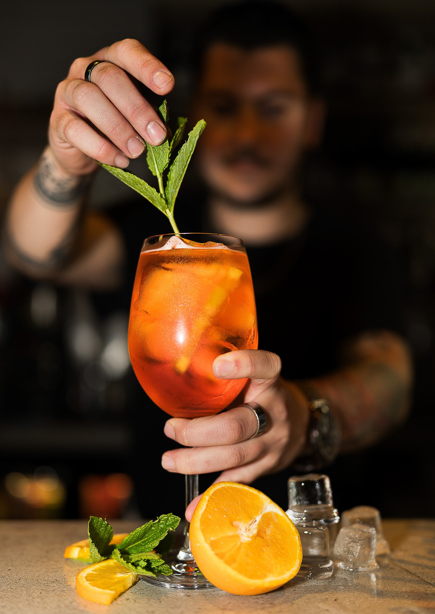 Bartender serving Aperol spritz cocktail with mint.