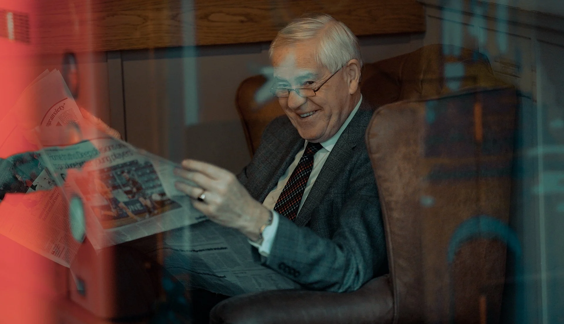 Older man in a suit smiling while reading a newspaper through a café window — Dublin street photography, Photo by Daniya.