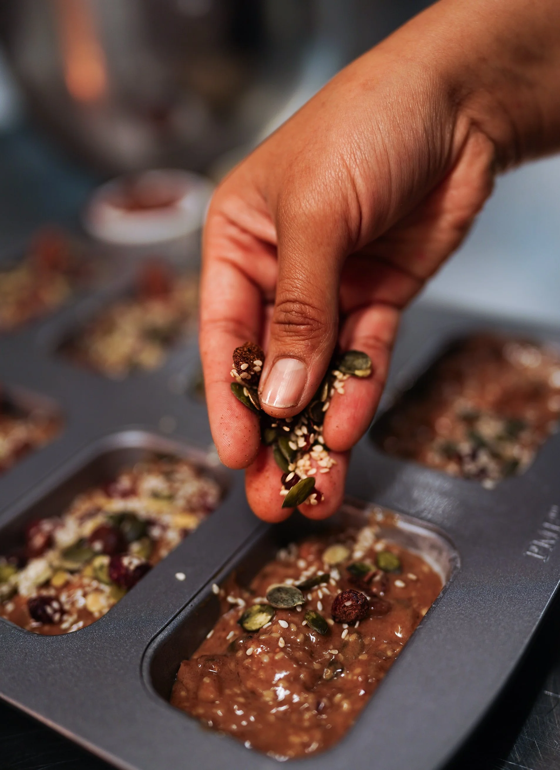 Hand sprinkling nuts over chocolate bars in café kitchen.