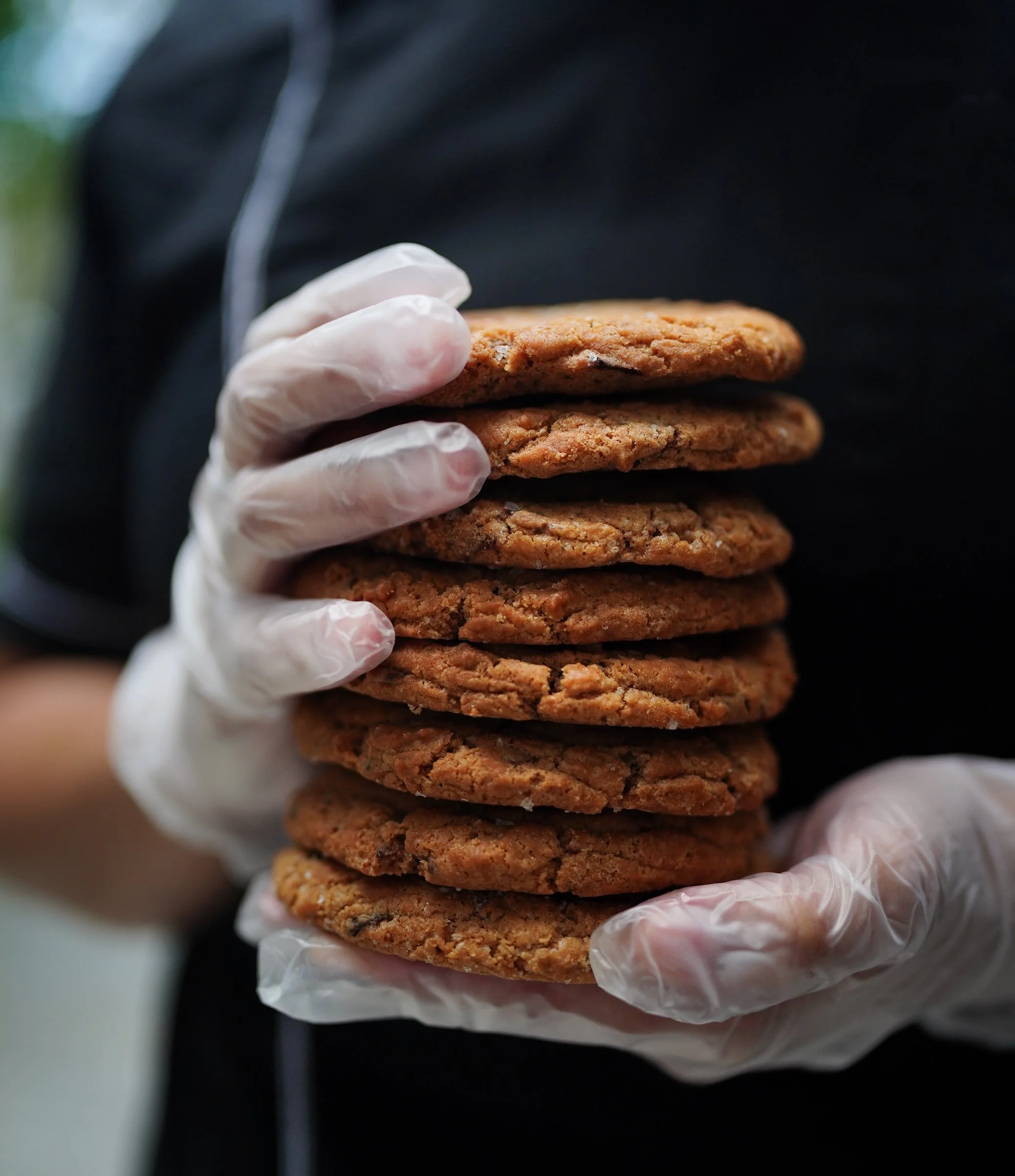 Chef holding stack of freshly baked cookies with gloves.