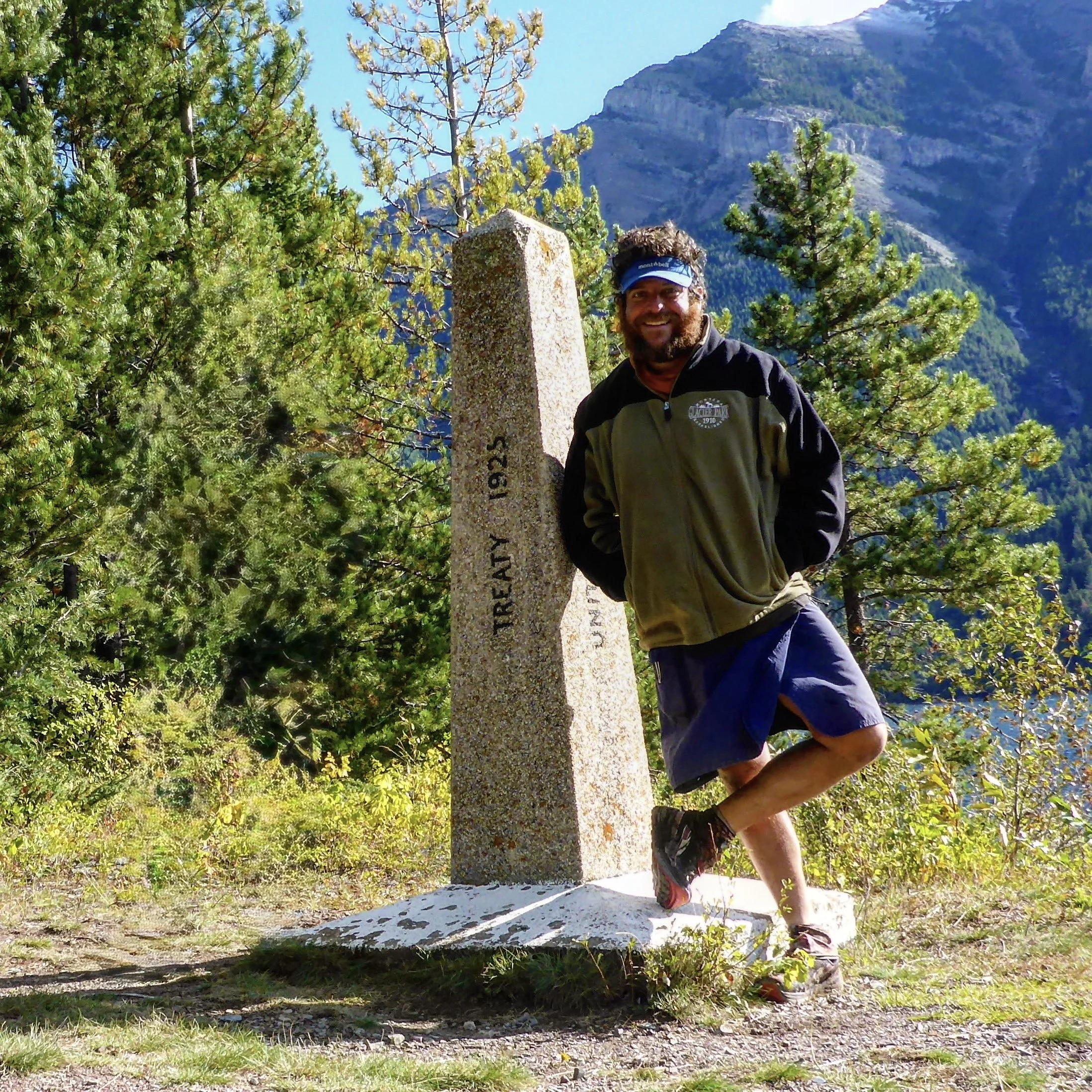 A hiker stands next to a stone obelisk in Glacier National Park at end of the Continental Divide Trail.
