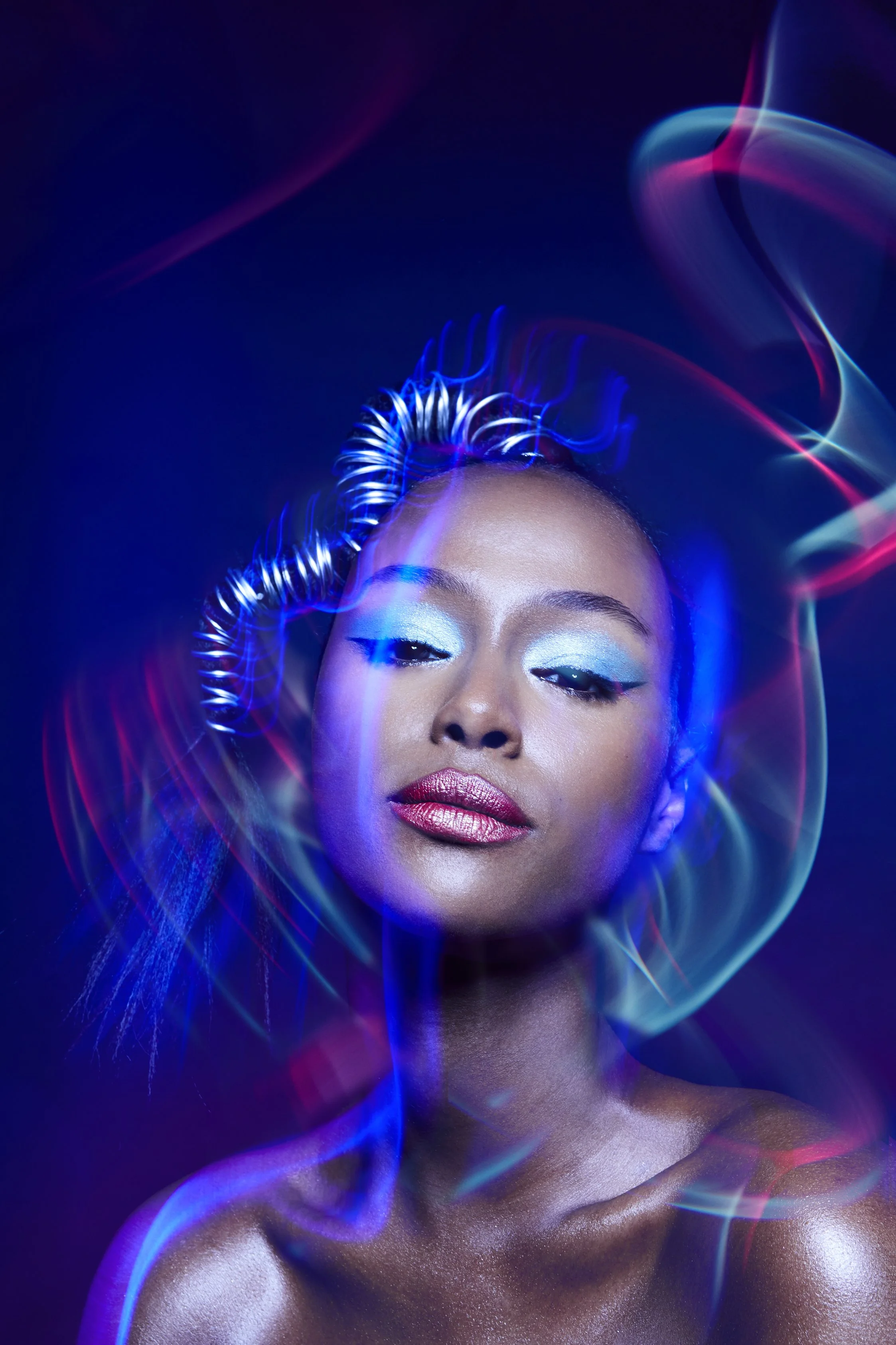 A cropped beauty image of a female model with blue makeup and coloured lights trails 