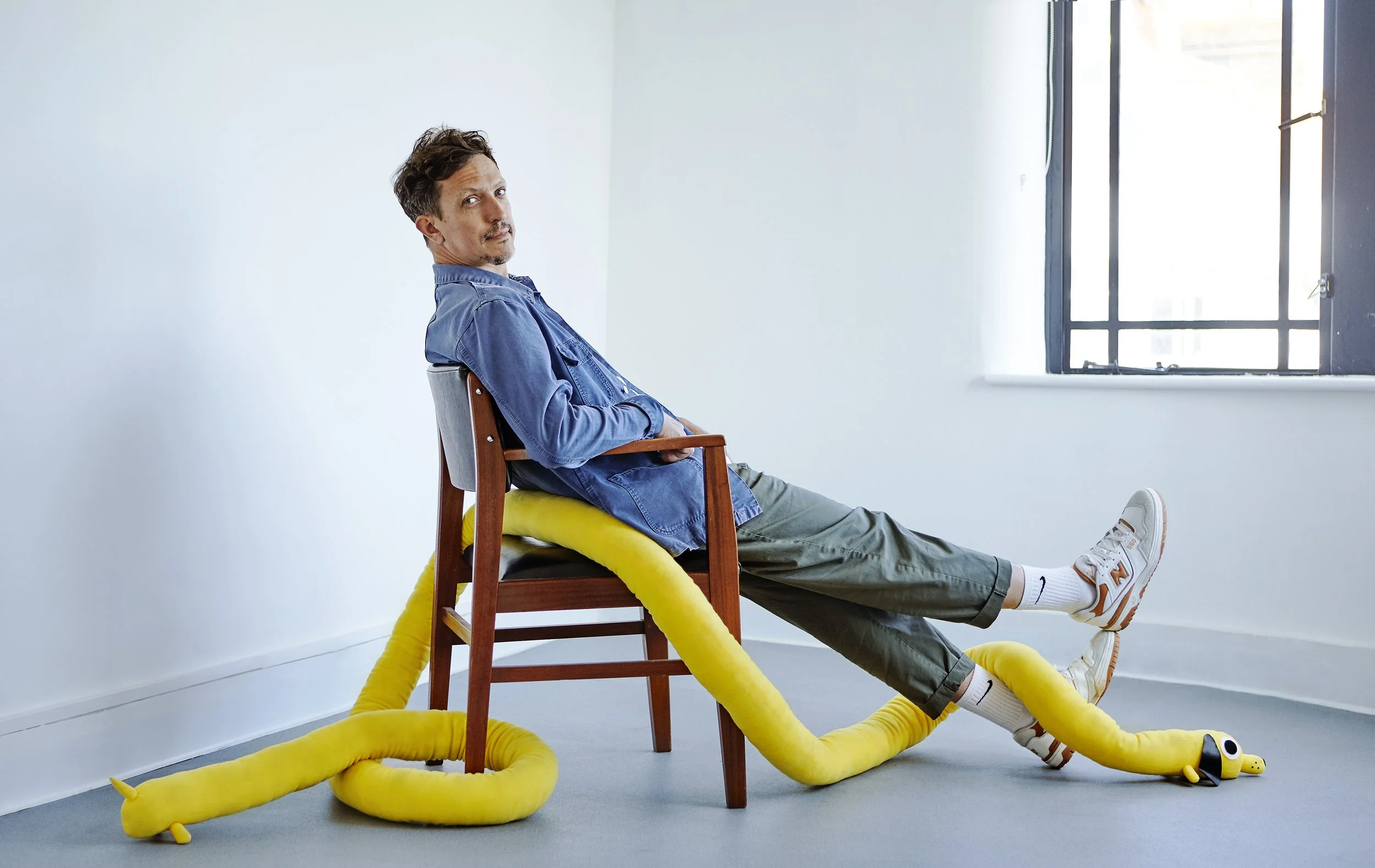 Portrait of white man with dark hair sitting side ways with extended legs and toy dog wrapped around chair