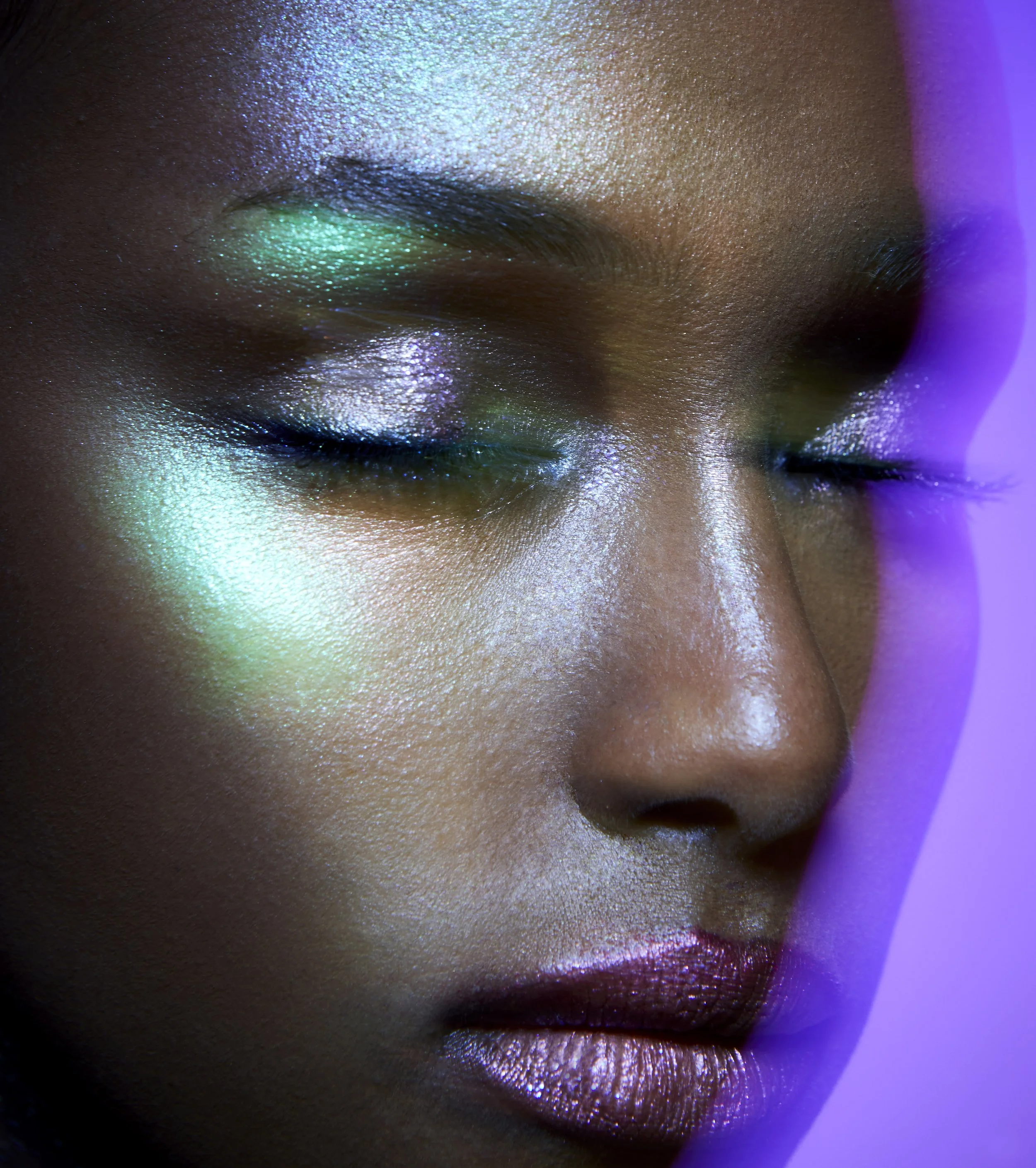 A cropped beauty image of a female model with silver and green makeup and purple background with a double exposure