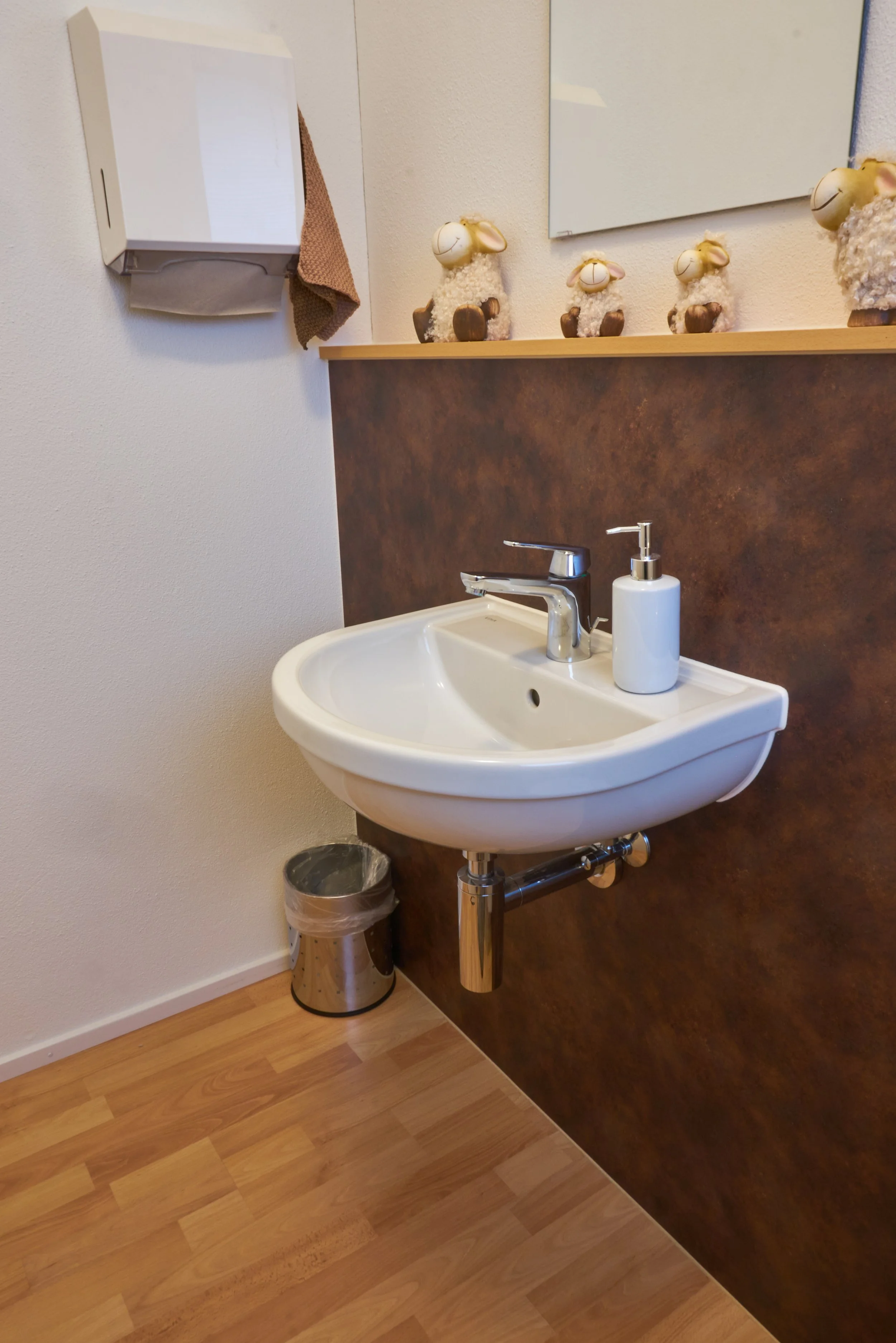 Waschbecken mit Seifenspender in einem Badezimmer, dekorative Schafe auf einem Holzregal