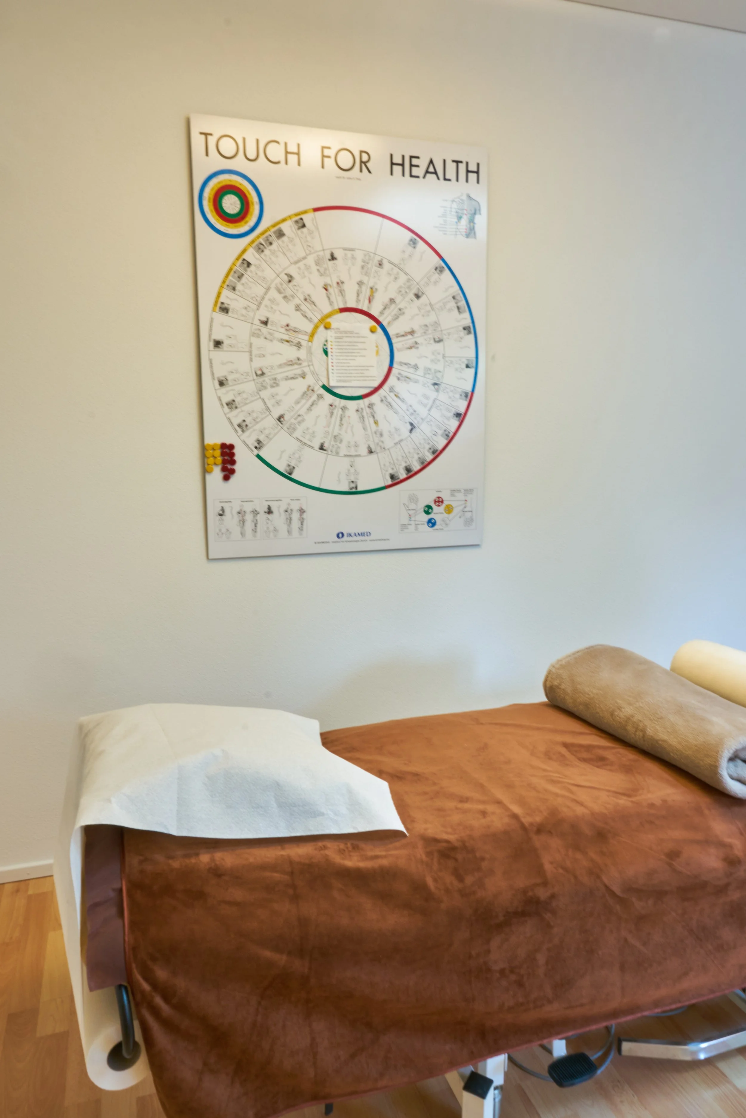 Behandlungsraum mit Massagebett, Handtuch, Rollkissen und einem Anatomie-Poster an der Wand