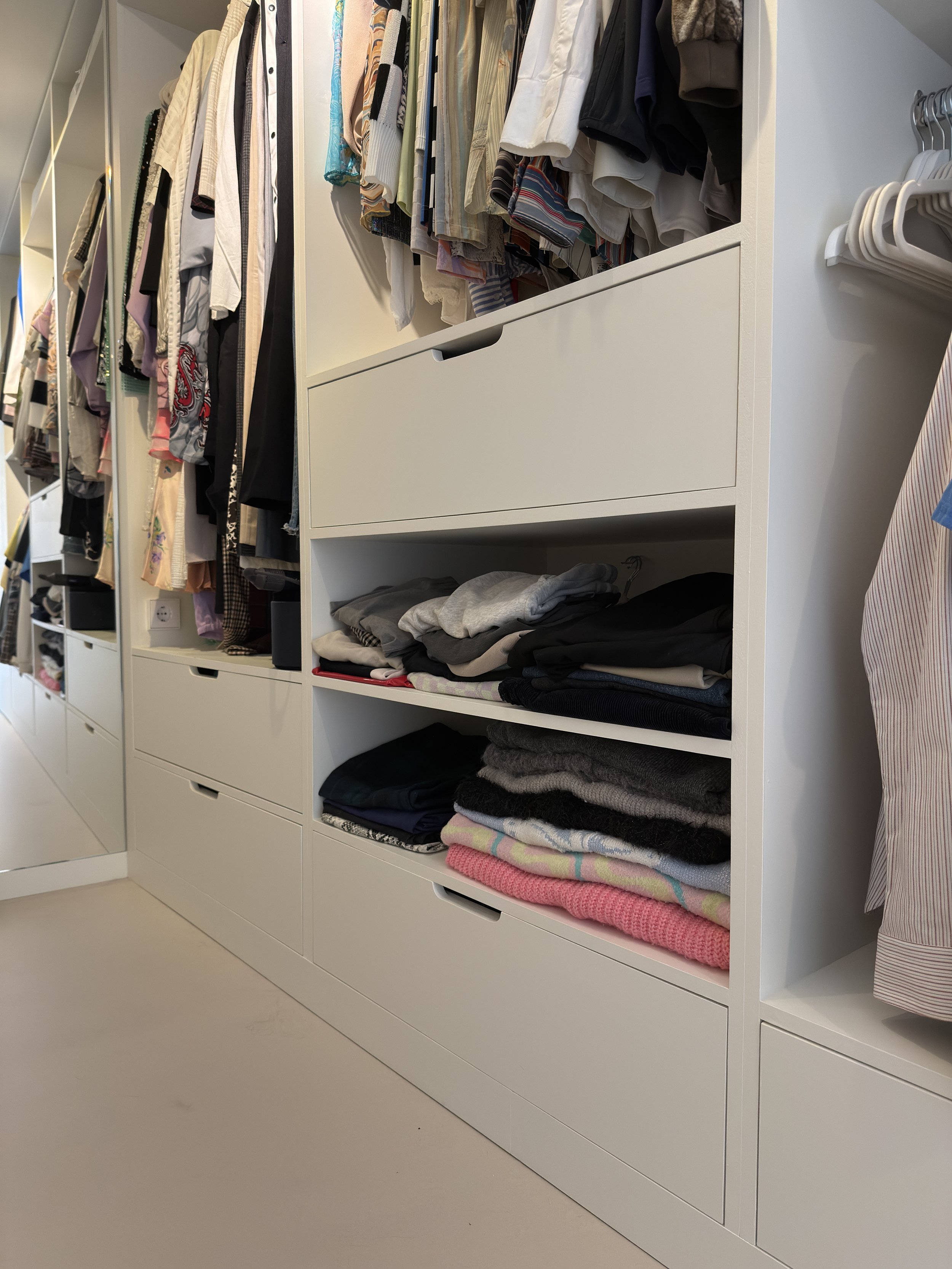 Inloopkast met kledingrekken en planken vol opgevouwen en opgehangen kleding.