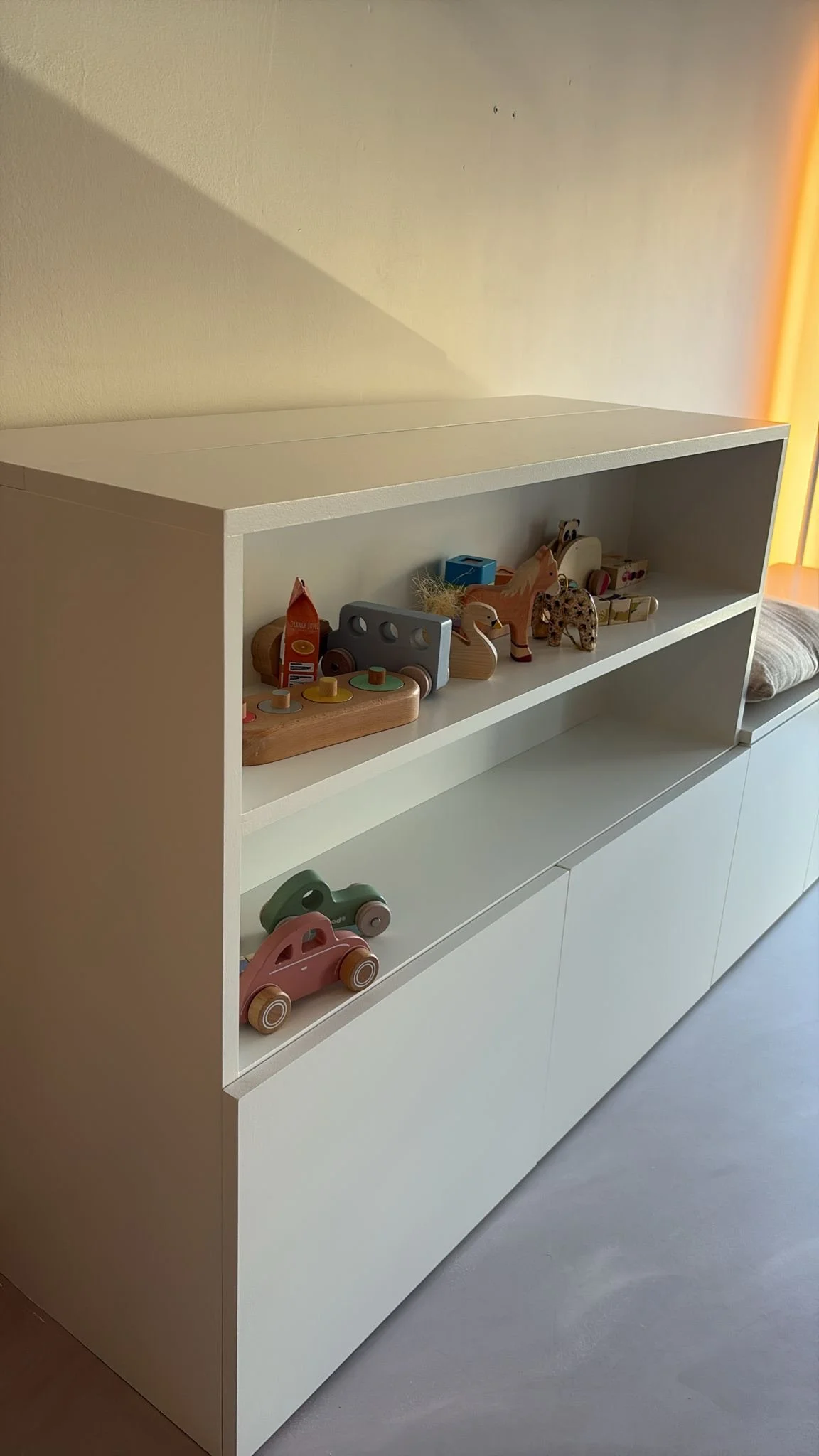 Witte kast met speelgoed, waaronder houten auto's en dieren