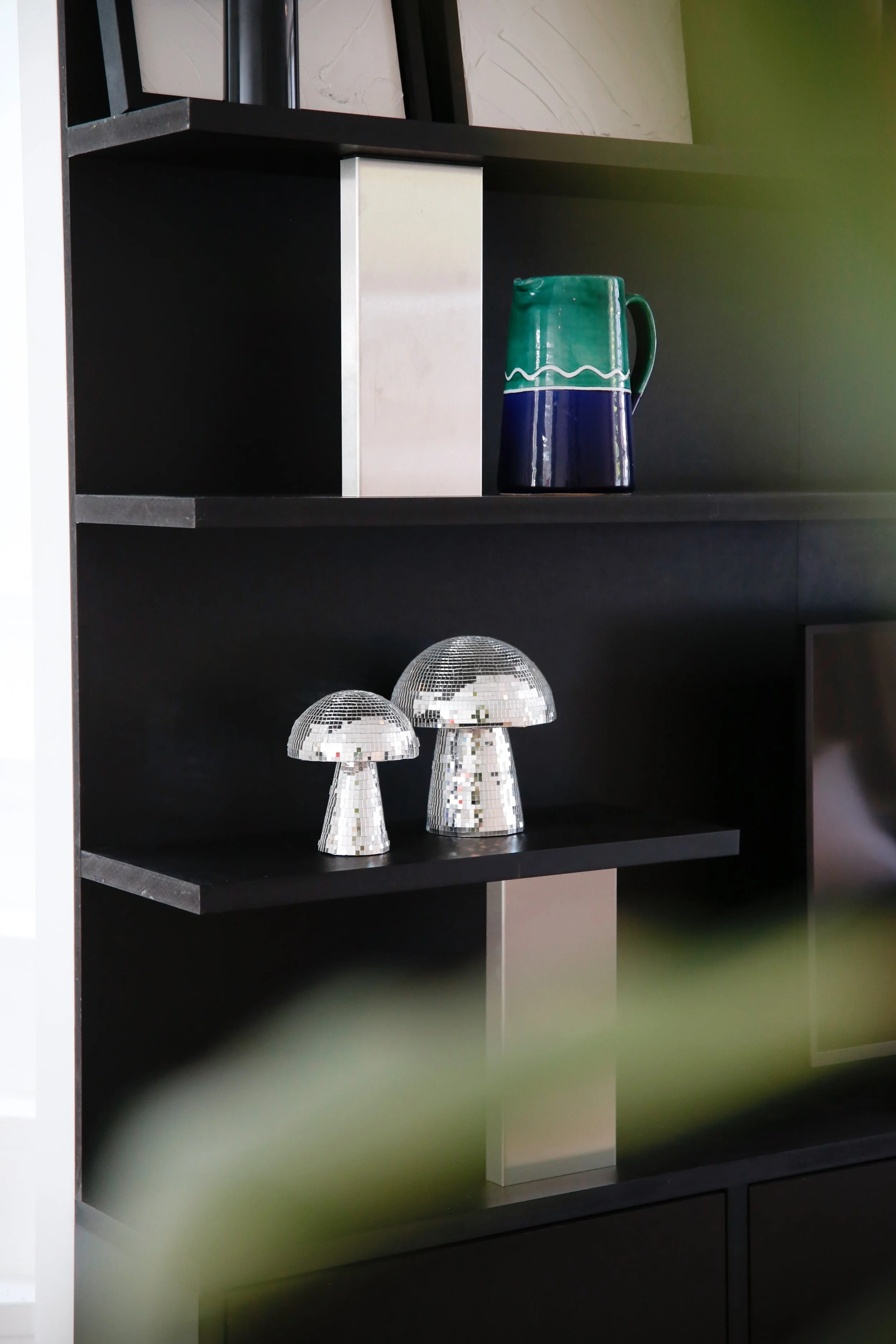 Decoratief interieur met keramische vaas en twee keramische paddenstoelen-spiegels op een zwarte open kast.