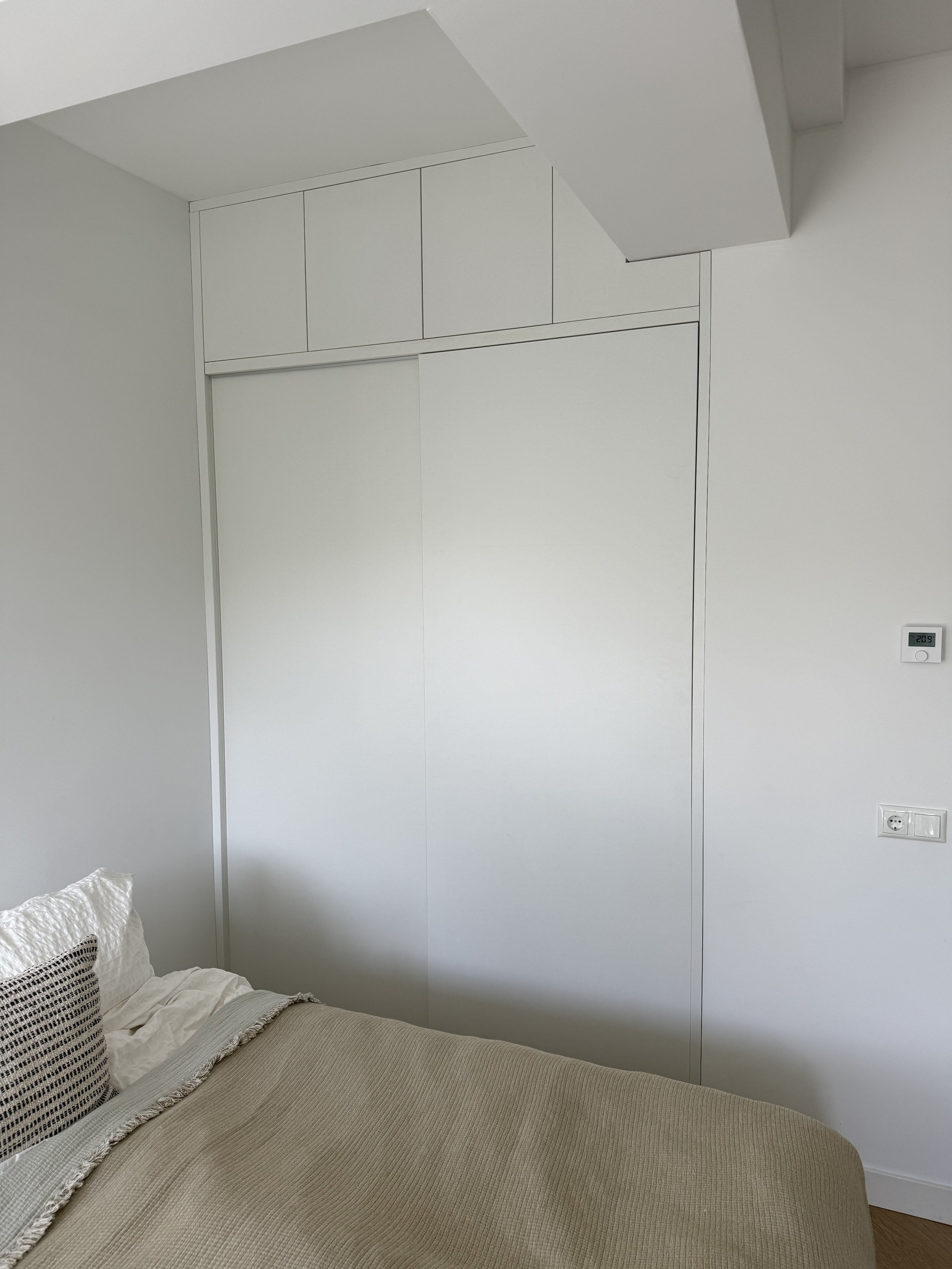 Een wit slaapkamer met een bed en een grote ingebouwde kast met schuifdeuren.