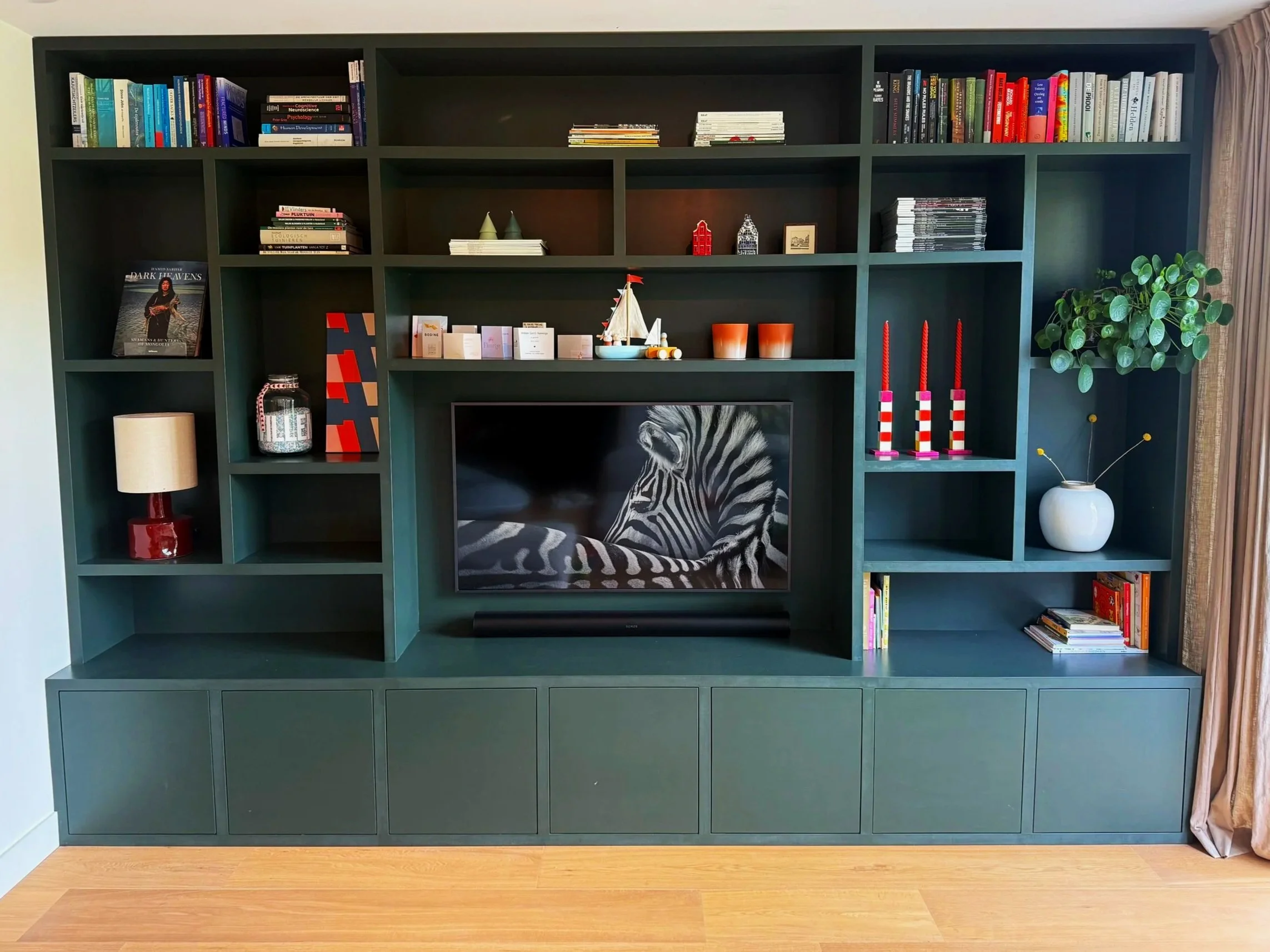 Donkere groene boekenwand met diverse boeken, decoratieve objecten, planten en een televisie met zebra afbeelding.