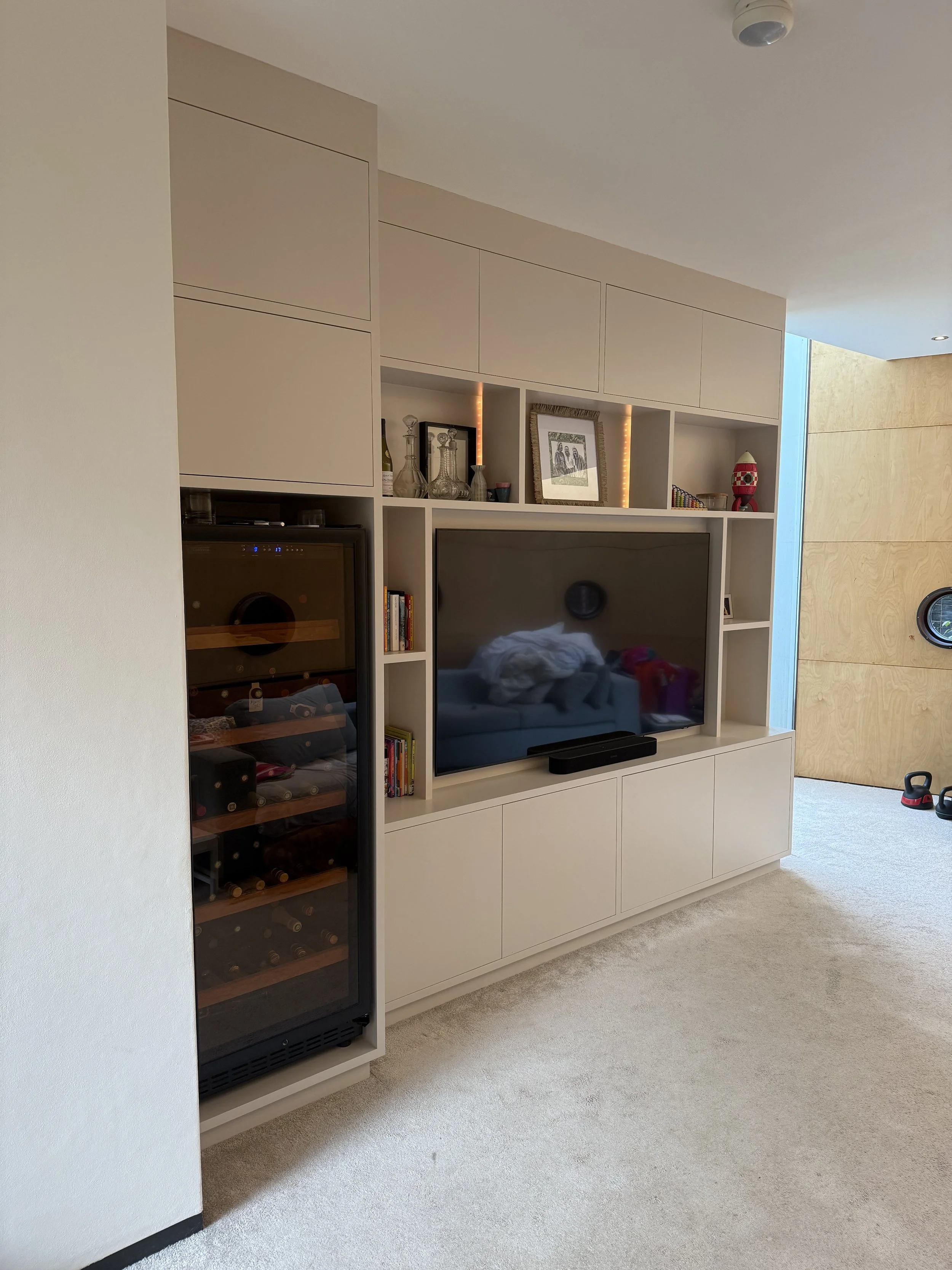 Woonkamer met witte muur, televisie, boeken, decoratieve items, wijnkast en een houten deur.