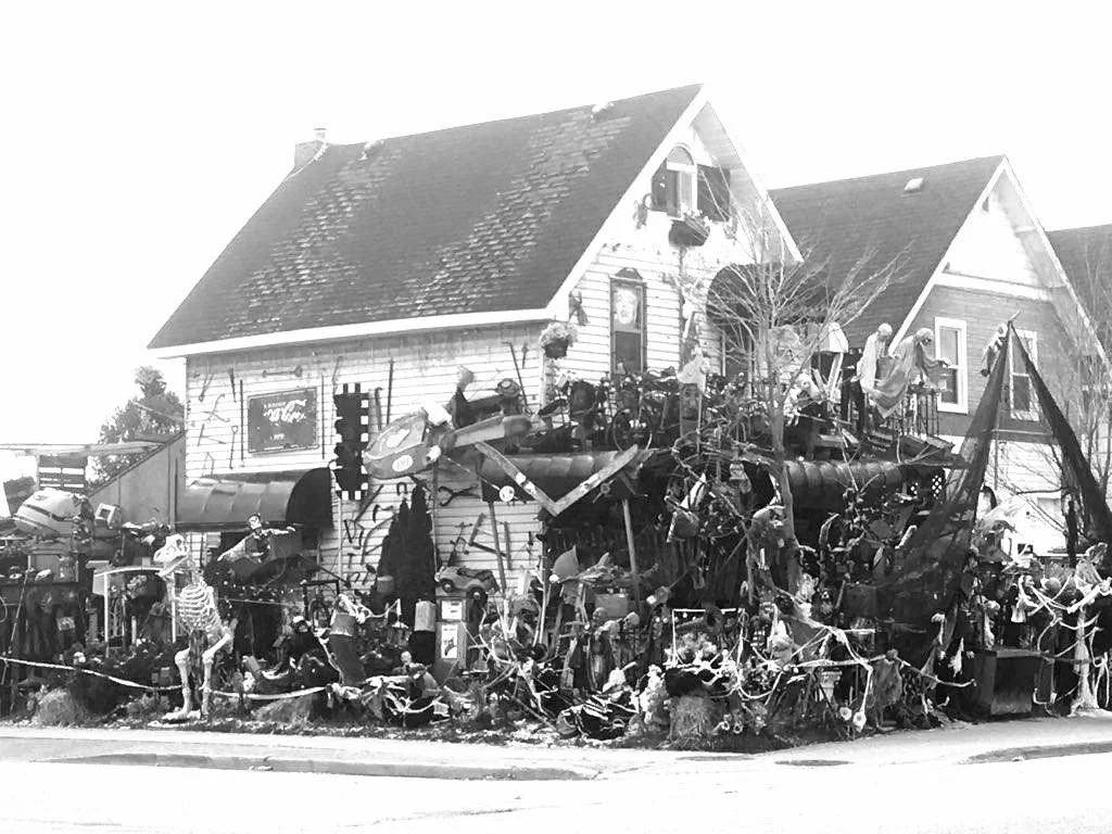 A house decorated with Halloween decorations, including skeletons, tombstones, and spooky themed items, with children in costumes outside.